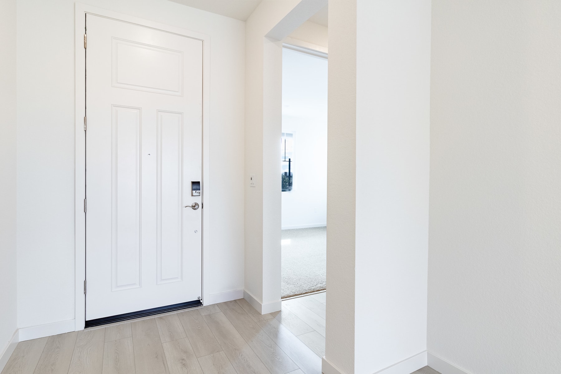 A white wooden door stands in a bright, minimalist hallway with light-colored hardwood floors and white walls.