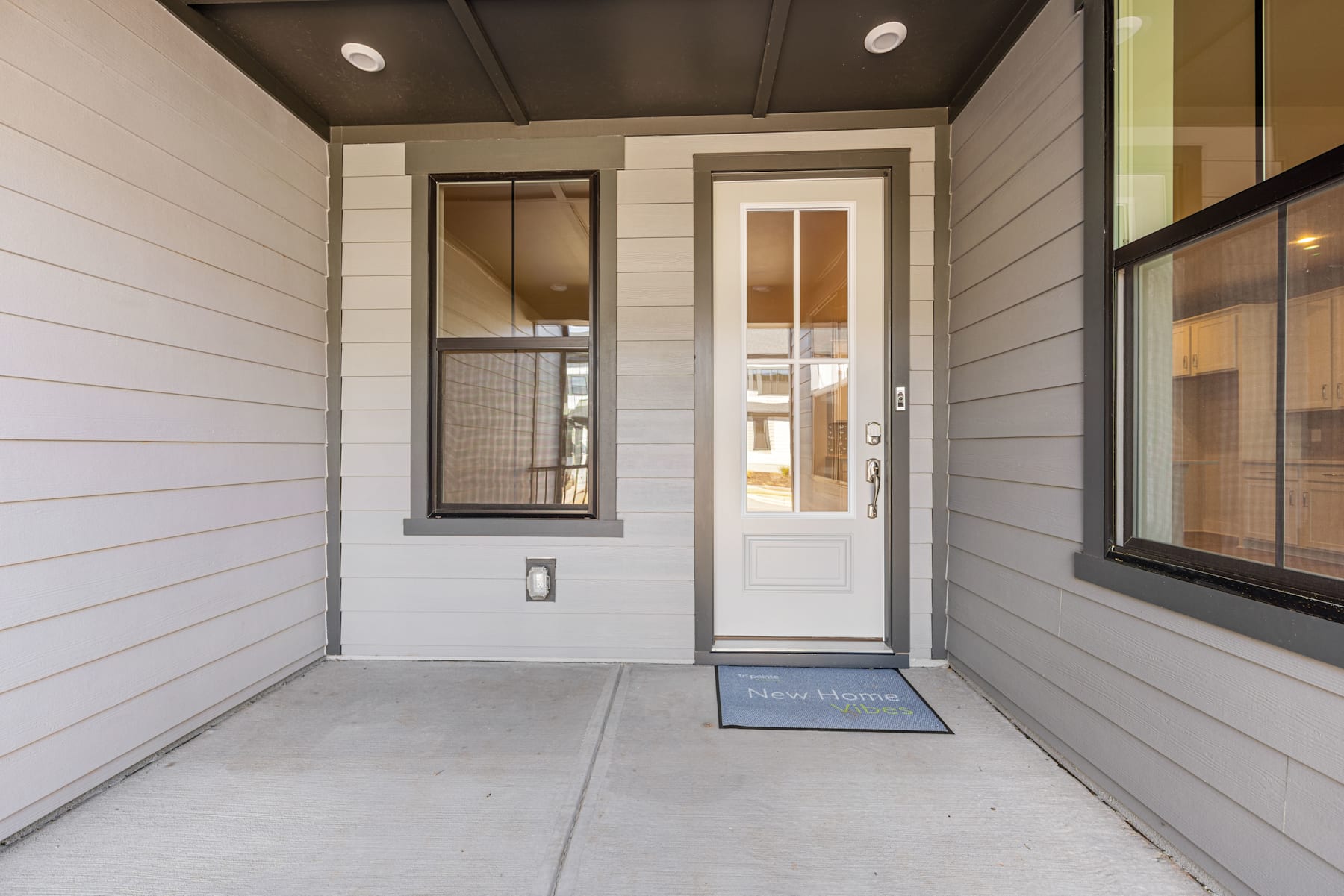 A modern, minimalist entryway with a white wooden exterior, a glass door, and a welcome mat on the concrete floor.