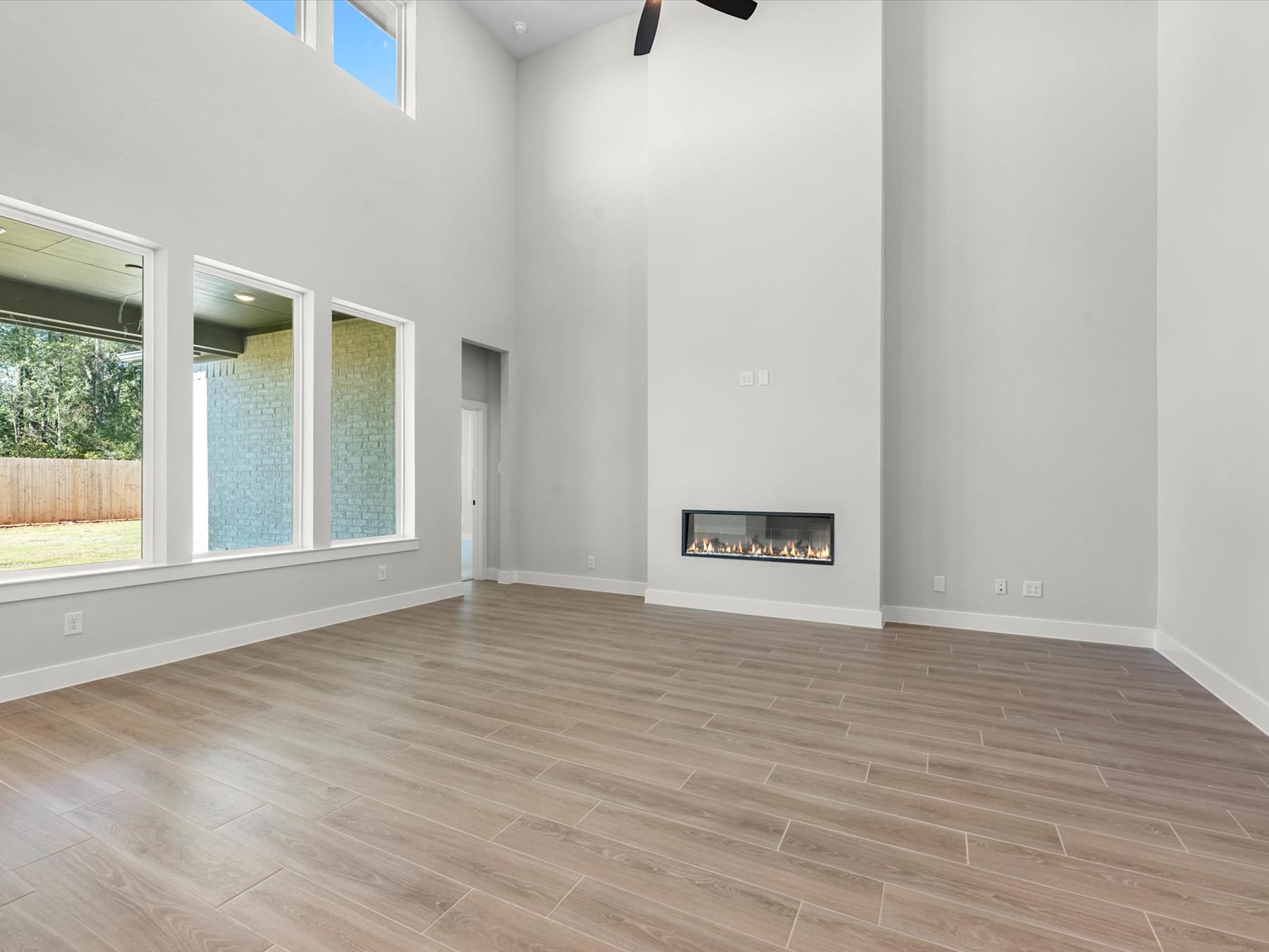 A spacious, modern living room with large windows, a fireplace, and a hardwood floor.
