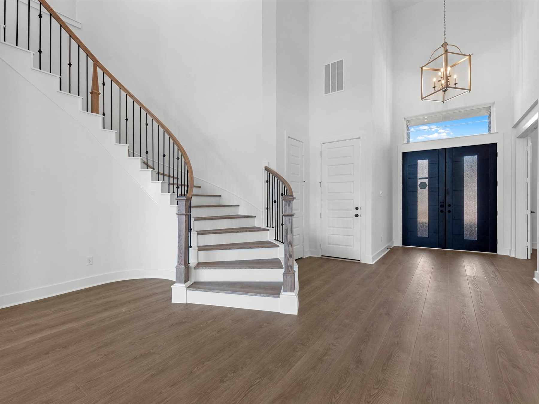 A spacious and bright entryway with a wooden staircase leading up, hardwood floors, and a decorative light fixture hanging from the ceiling.
