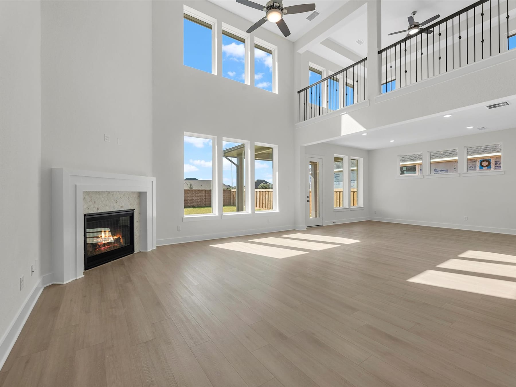 A spacious and bright living room with a high ceiling, hardwood floors, and a fireplace, surrounded by large windows that let in natural light.