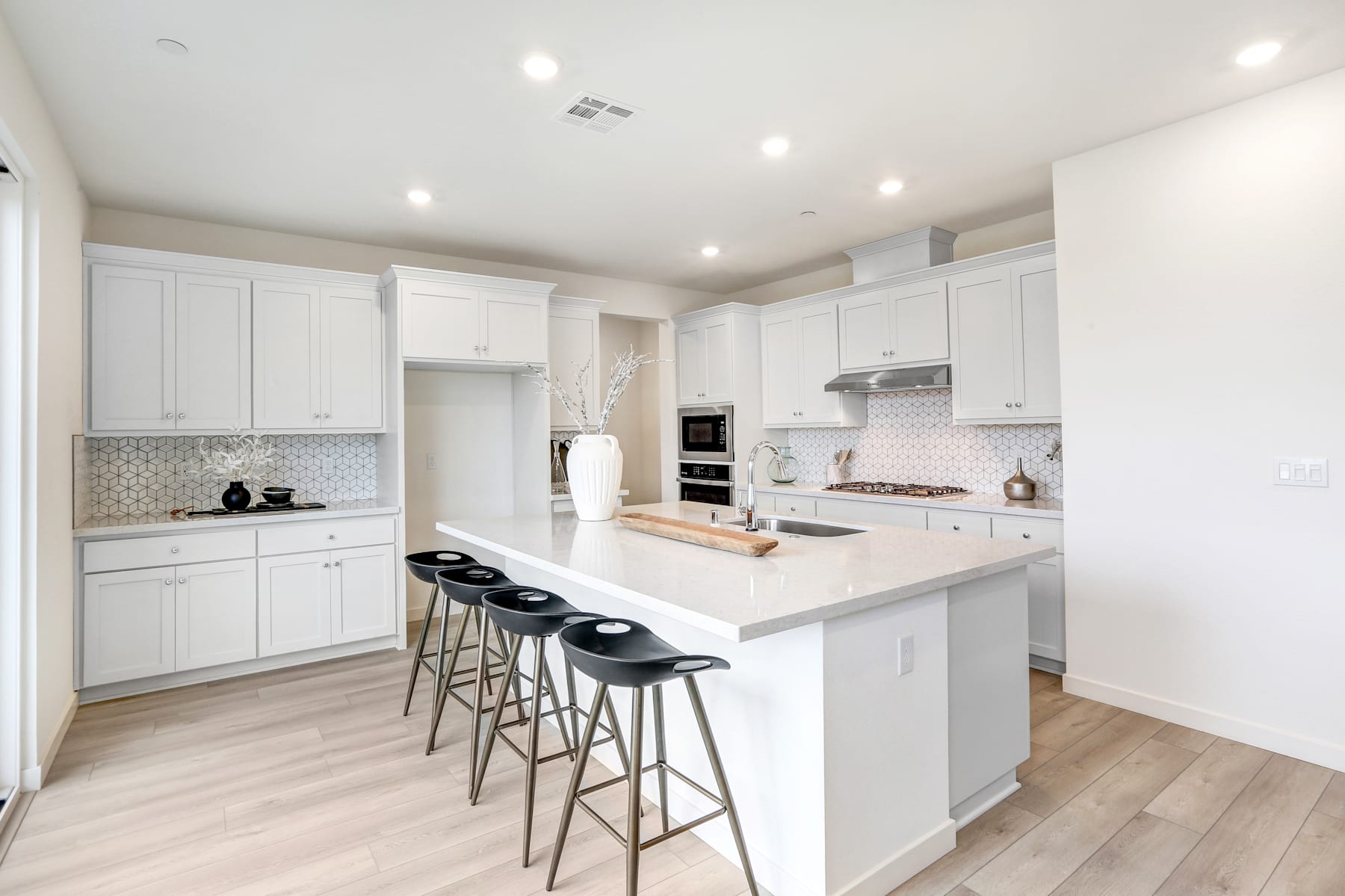 A modern, bright, and spacious kitchen with white cabinets, a large island with bar stools, and hardwood floors.
