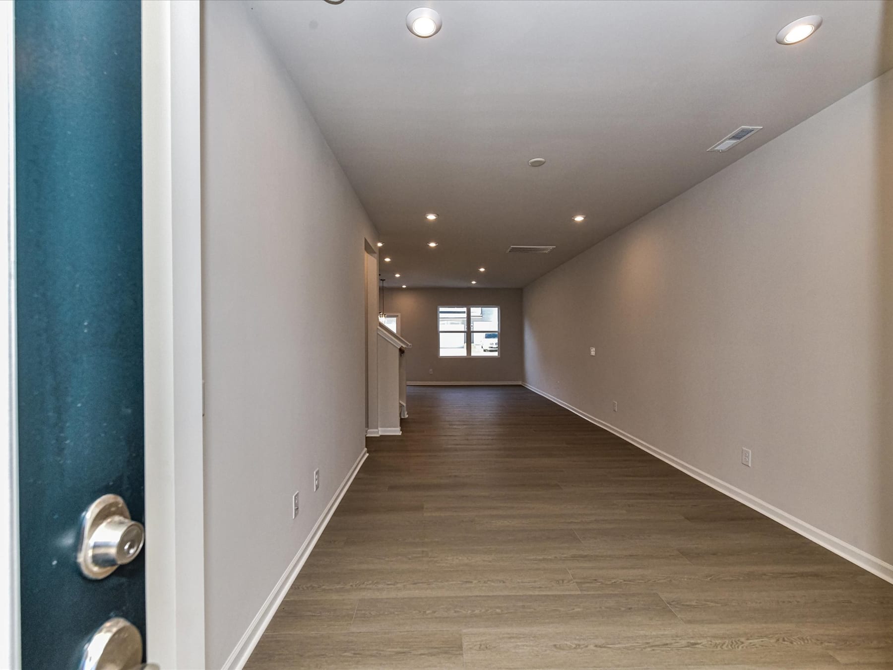 A long, well-lit hallway with a wooden floor and recessed lighting in the ceiling.