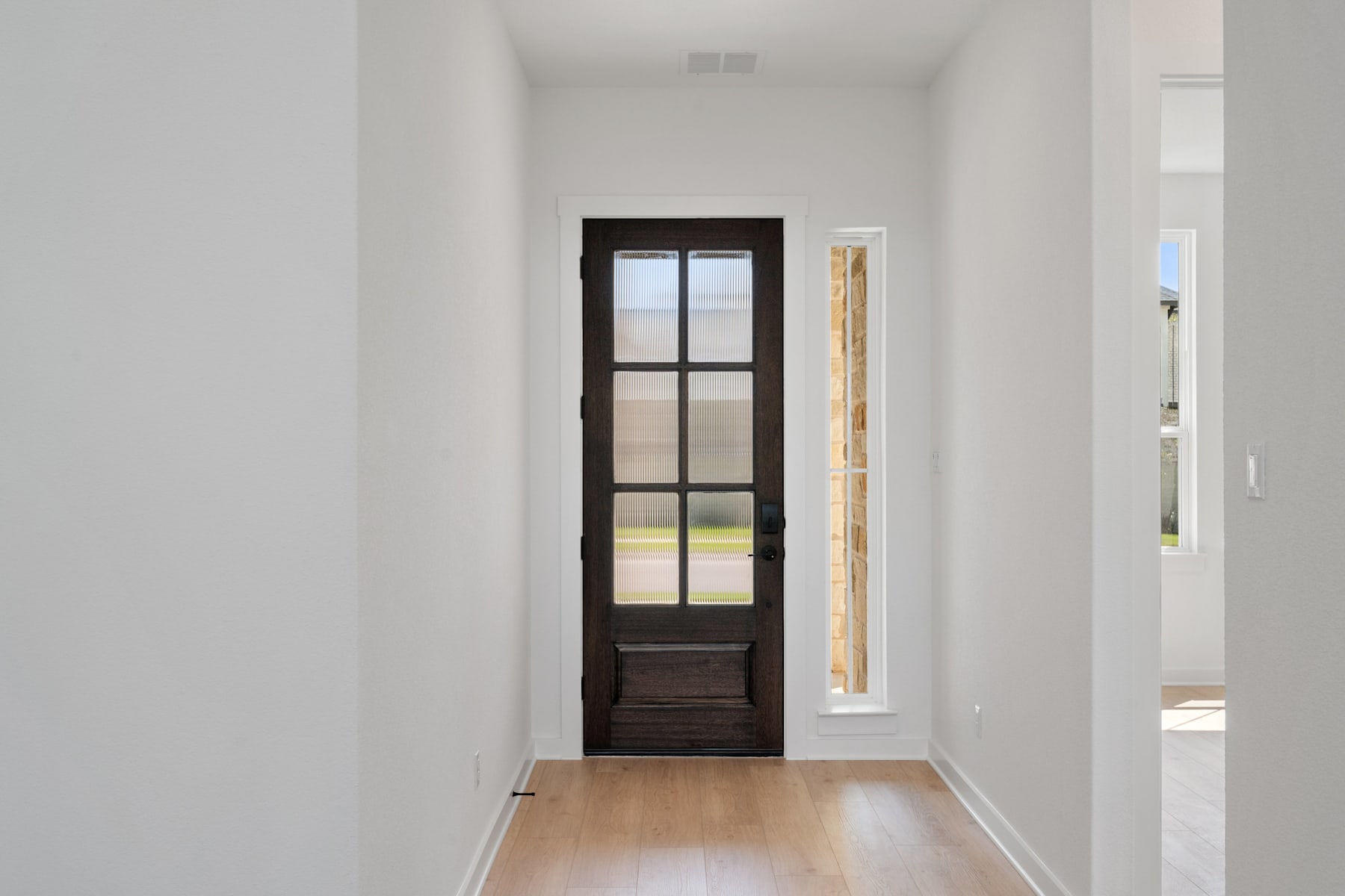 A bright, minimalist hallway with a wooden door and a narrow window, leading to an outdoor view.