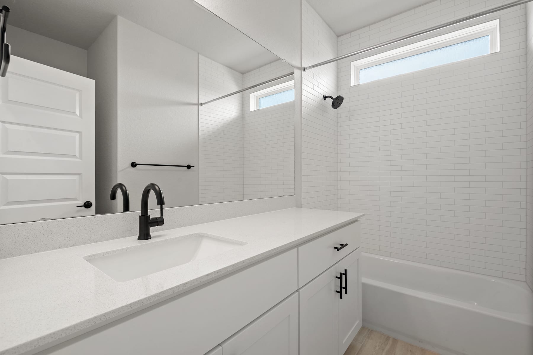 A modern, minimalist bathroom with white walls, a large vanity, and black fixtures, creating a clean and sleek aesthetic.