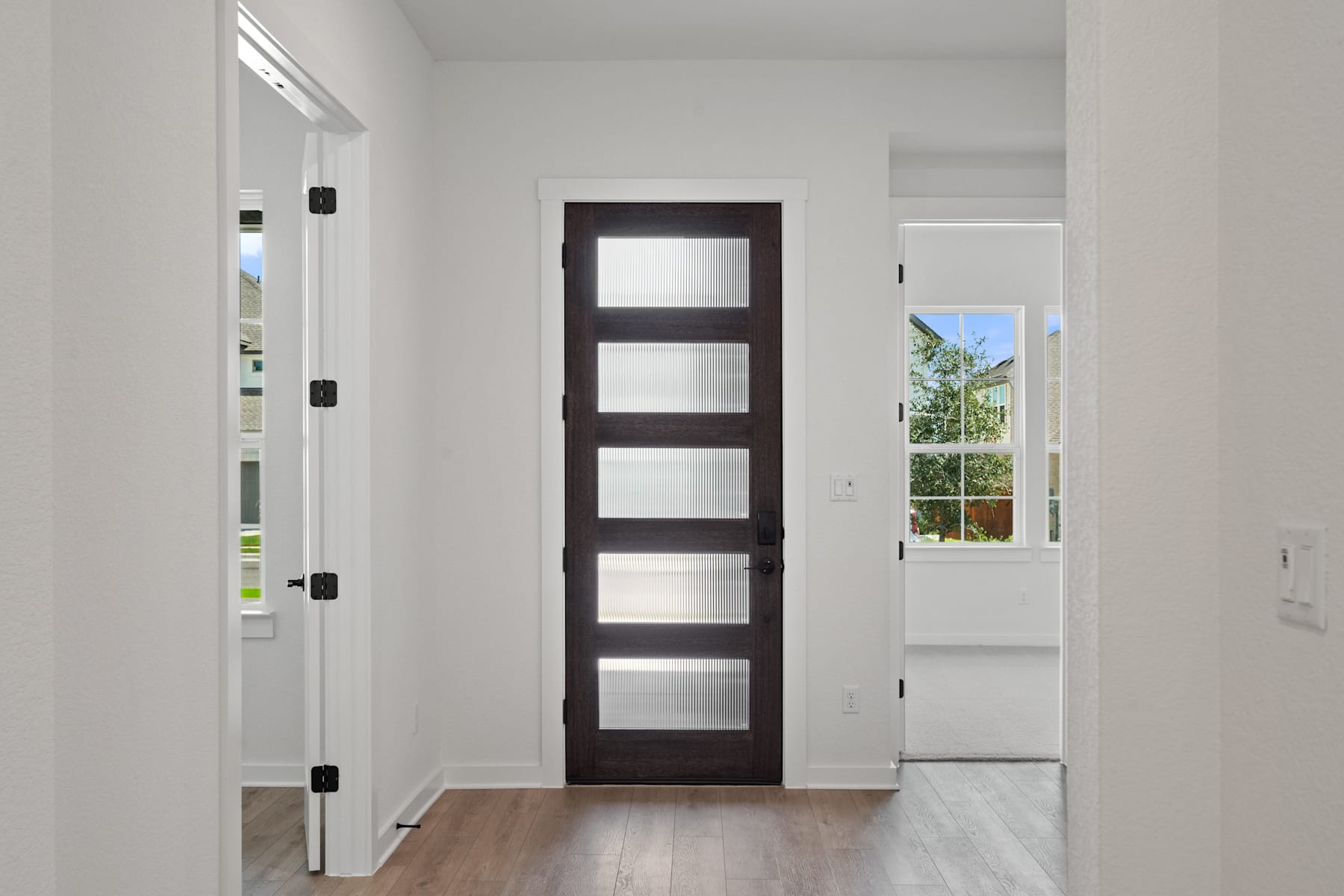 A modern, minimalist interior with a dark wooden door featuring multiple glass panels, set against a bright, airy background with a window visible.