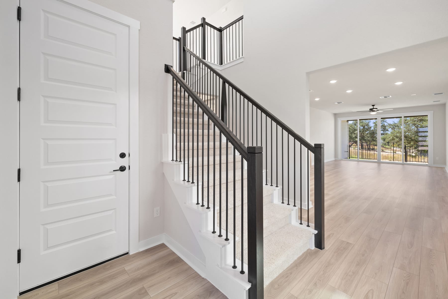 A modern, minimalist entryway with a white door, a sleek black metal staircase railing, and a bright, open space with hardwood floors.
