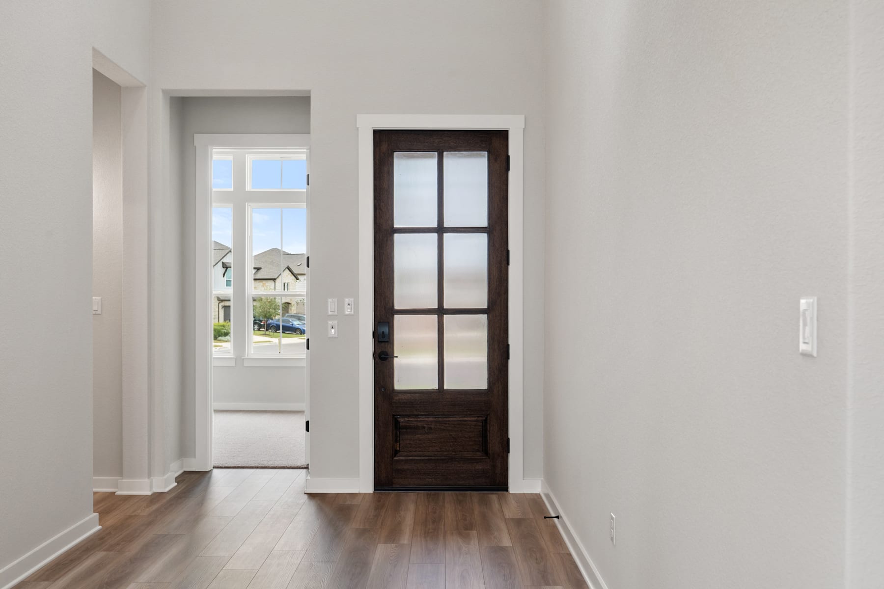 A bright, airy hallway with a wooden door leading to the outdoors, featuring a hardwood floor and white walls.