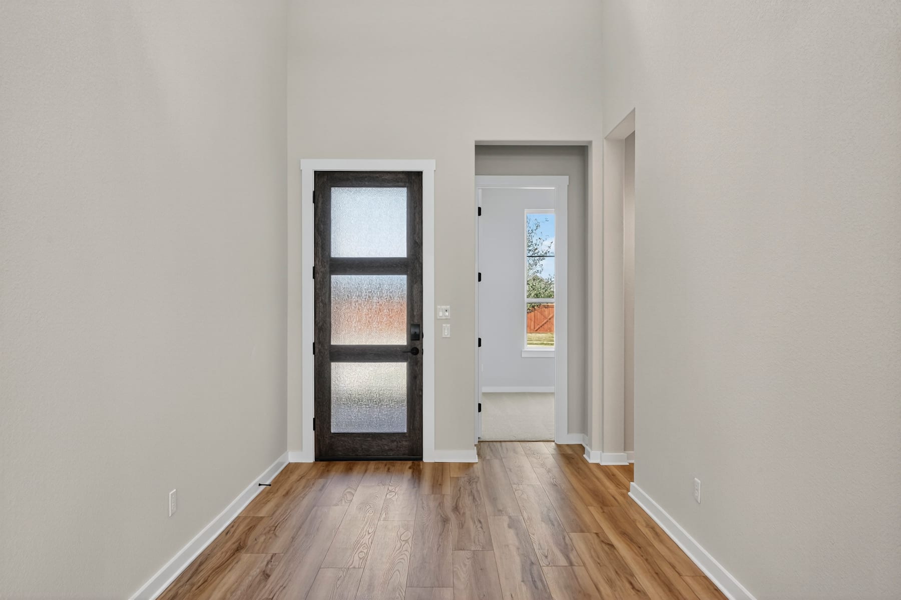 A bright, minimalist hallway with a wooden floor and a glass-paneled door leading to the outdoors.