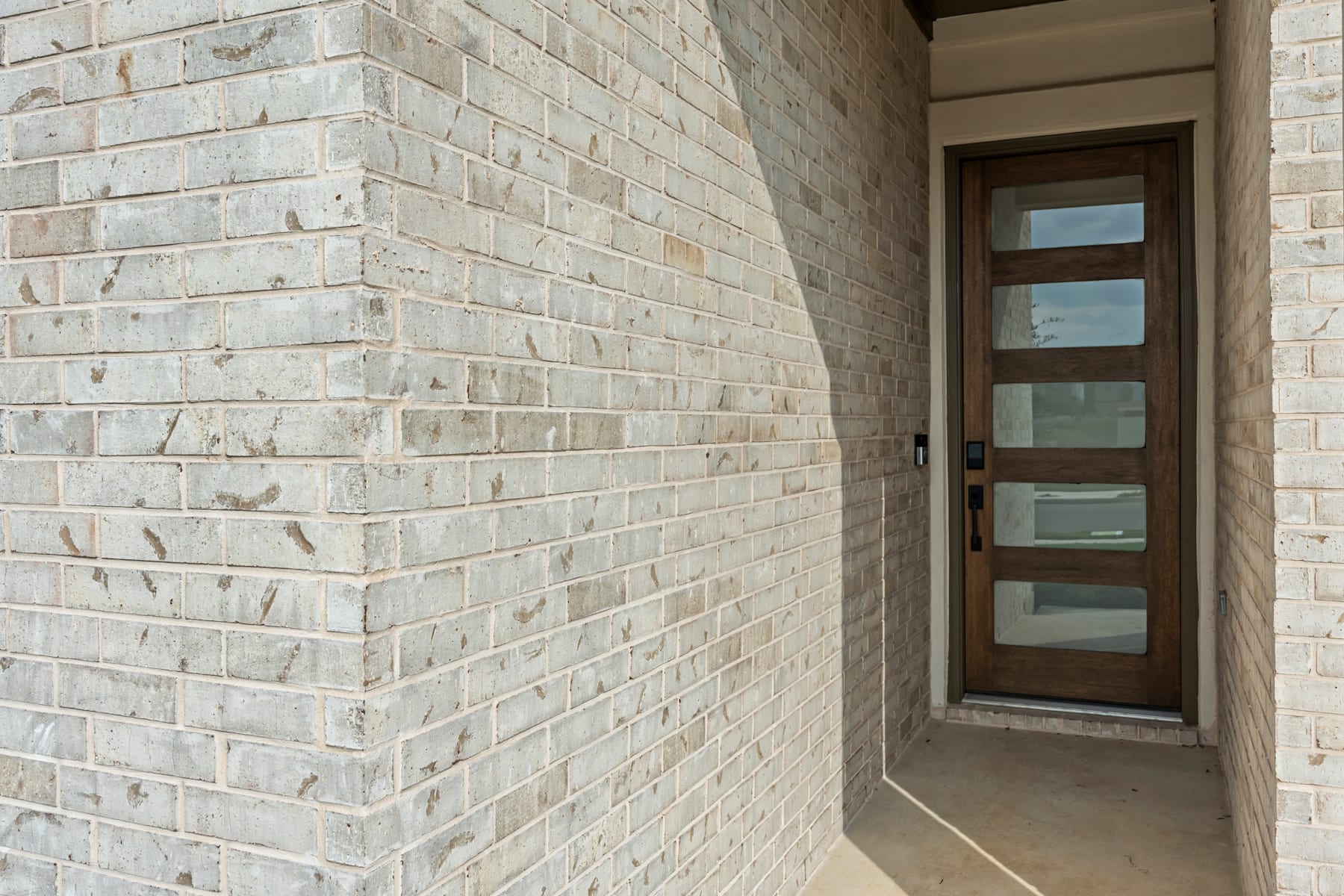 The image shows a brick wall with a wooden door and glass panels, leading to an interior space.