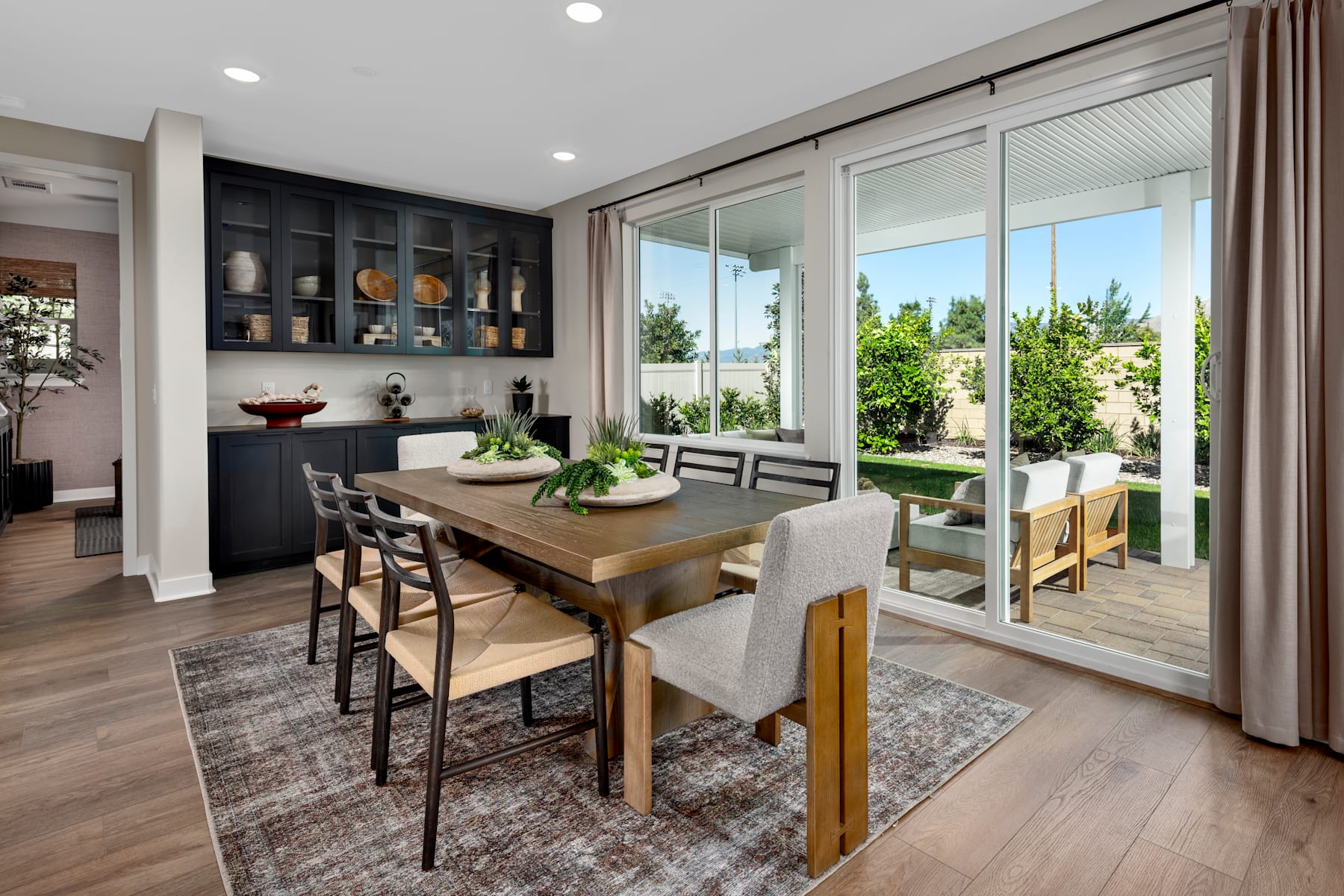 A modern and spacious dining area with a wooden table, upholstered chairs, and a large window overlooking a lush outdoor landscape.