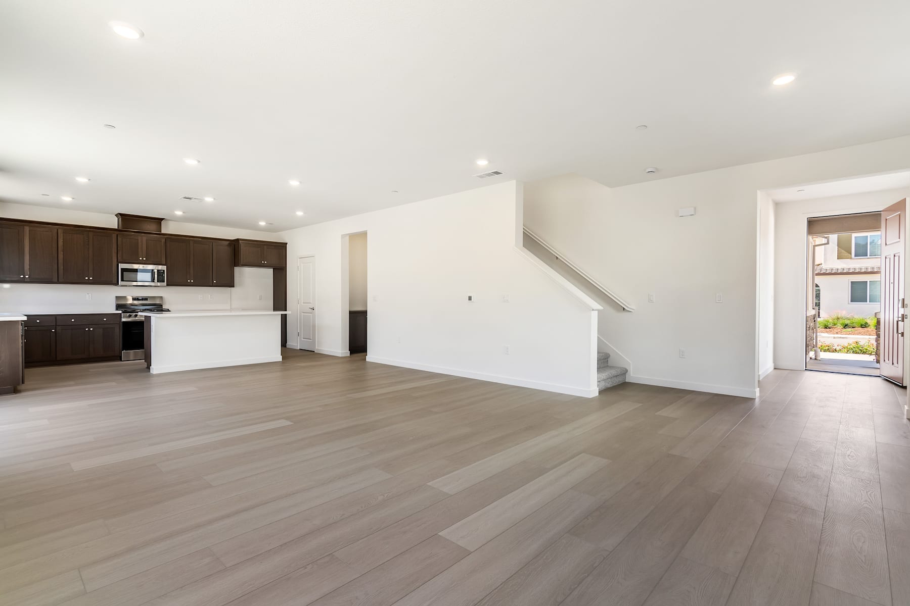 A spacious and modern open-plan living area with a kitchen, hardwood floors, and a staircase leading to an upper level.