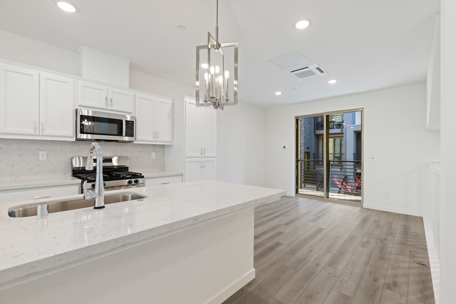 A modern, open-concept kitchen with white cabinets, a sleek countertop, and a chandelier overhead, leading into a spacious living area with hardwood floors.