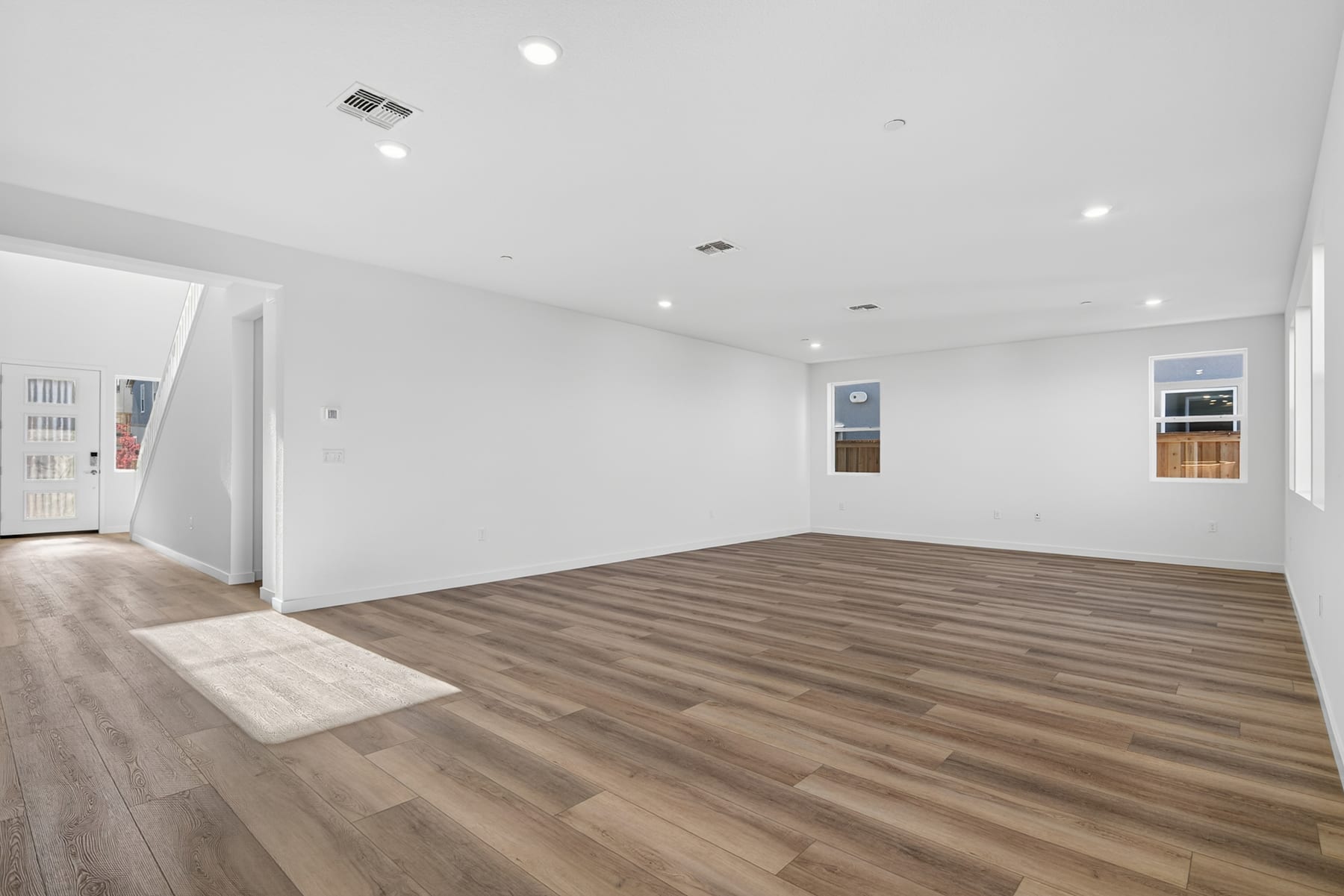 A spacious, well-lit room with a hardwood floor and recessed lighting, featuring a doorway leading to another area.