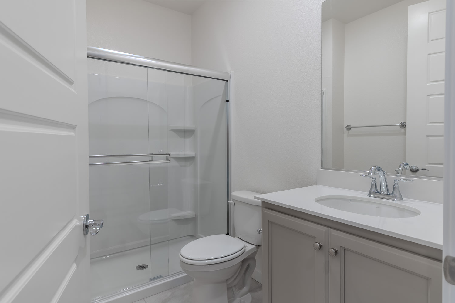 A modern, minimalist bathroom with a white vanity, a toilet, and a glass-enclosed shower.
