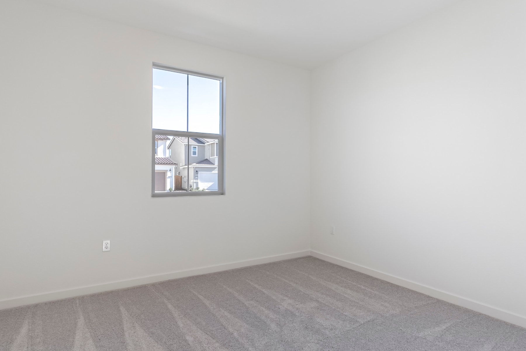 A simple, minimalist room with a large window, white walls, and a gray hardwood floor.