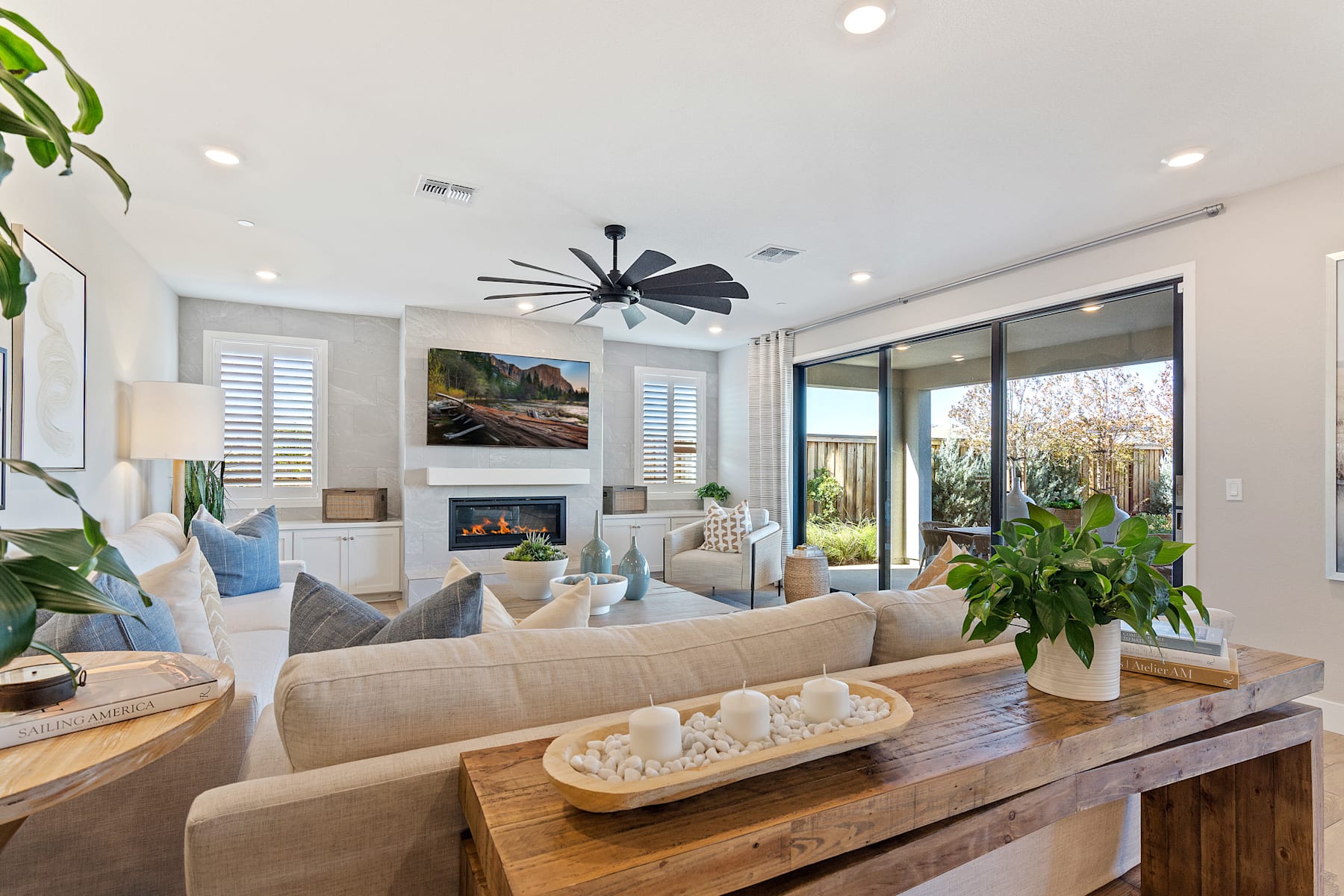 A cozy and inviting living room with a large sectional sofa, a fireplace, and a large window overlooking a lush outdoor space.