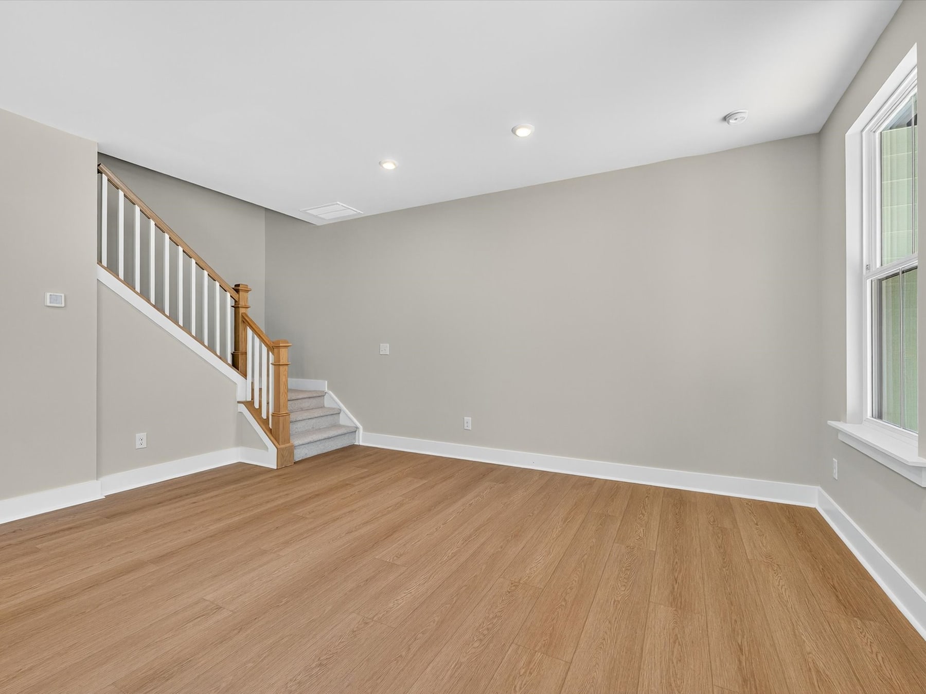 An empty room with light-colored walls, a wooden staircase, and a hardwood floor.