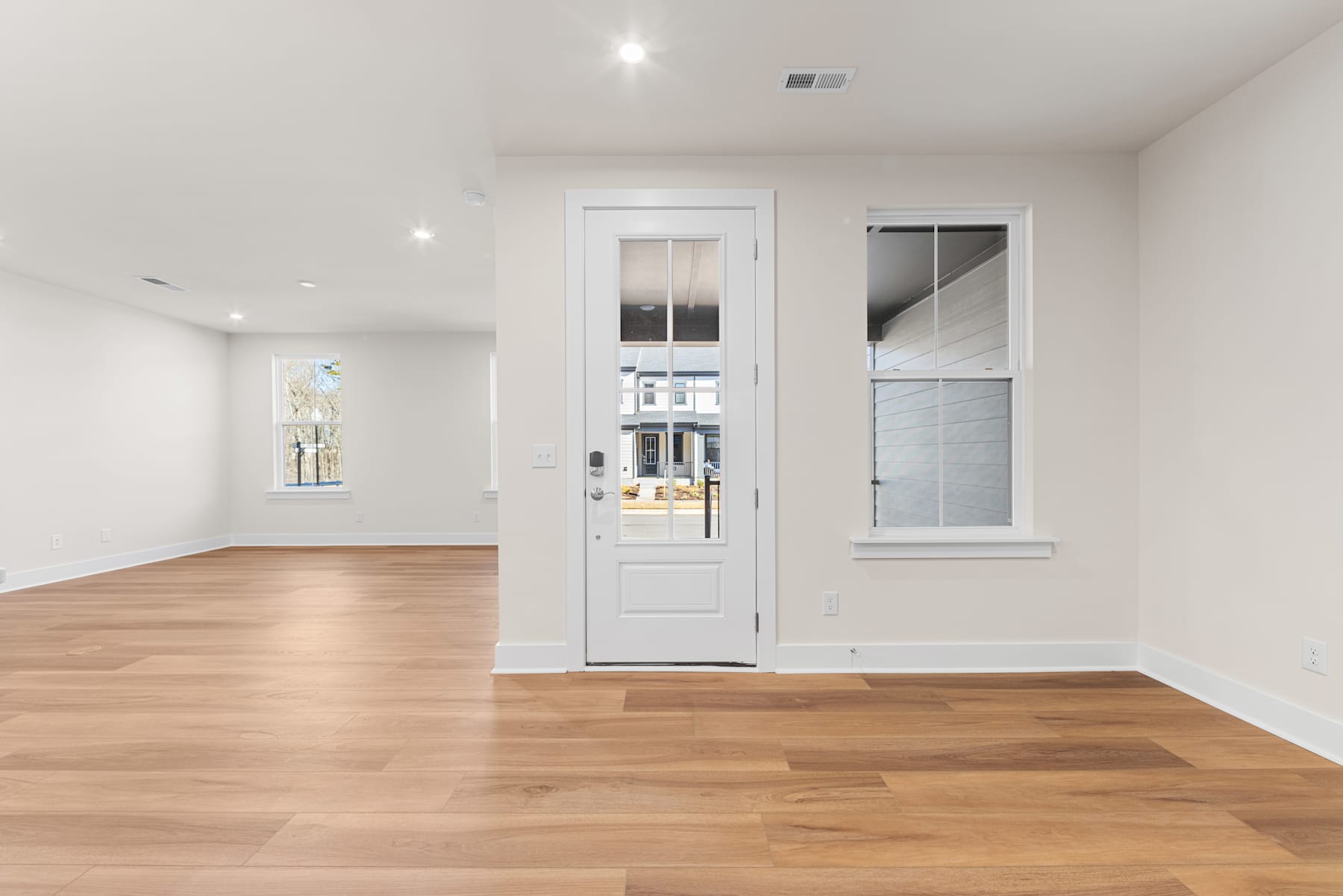 A spacious, well-lit room with a wooden floor, a white door, and a window overlooking the exterior.