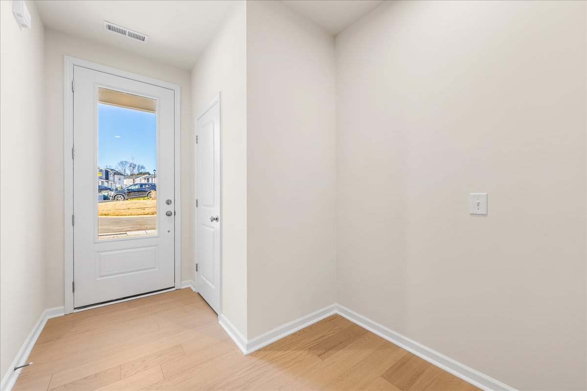 A bright, minimalist hallway with a white door leading to a view of the outdoors, and hardwood floors.