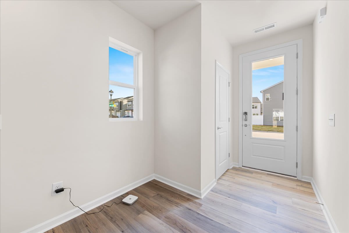 A bright and airy entryway with a white door leading to the exterior, and a hardwood floor extending into the space.