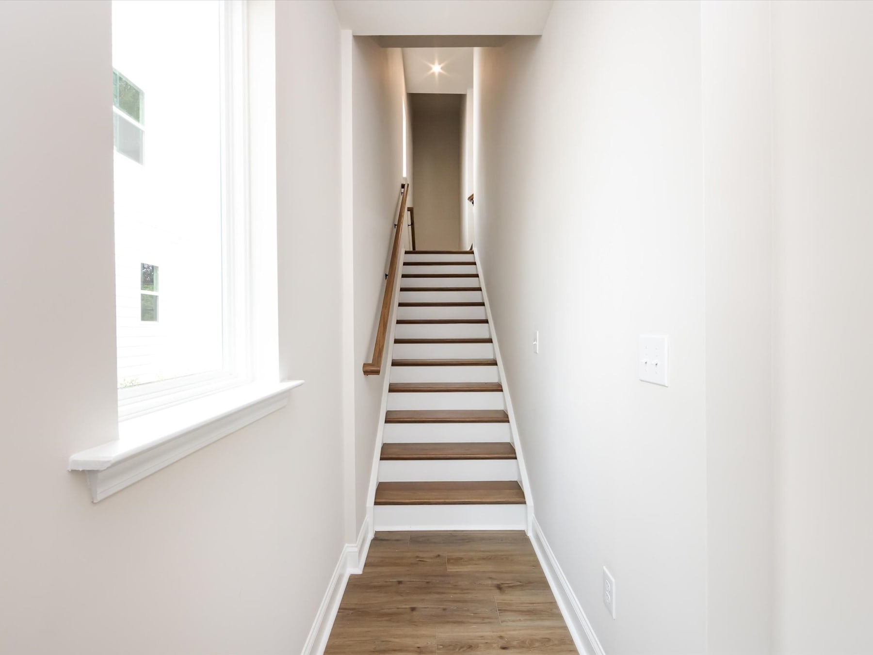 A bright, minimalist hallway with a wooden staircase leading up to a star-shaped light fixture on the ceiling.