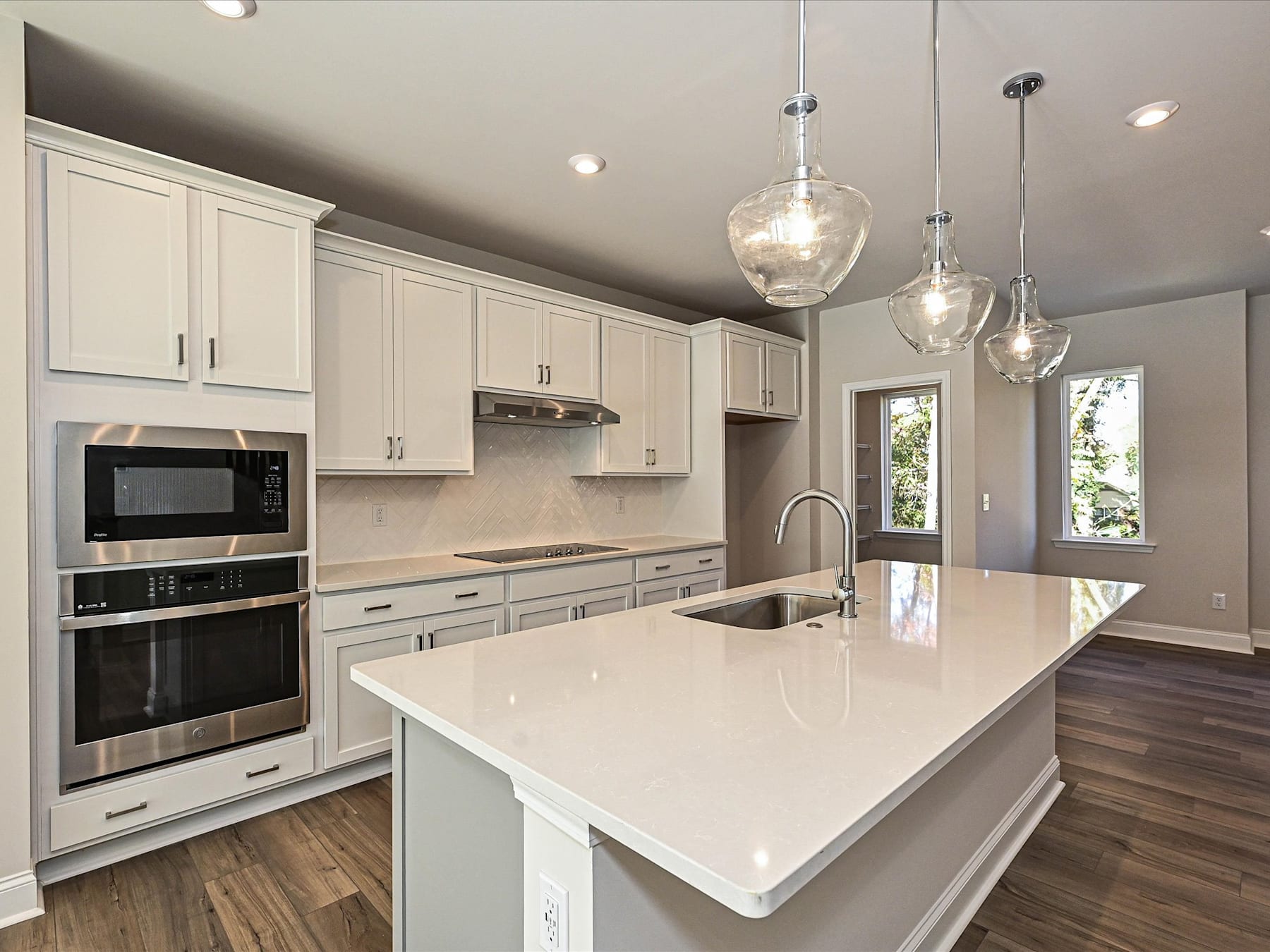 A modern, well-lit kitchen with white cabinets, a large island with a white countertop, and pendant lights hanging above.