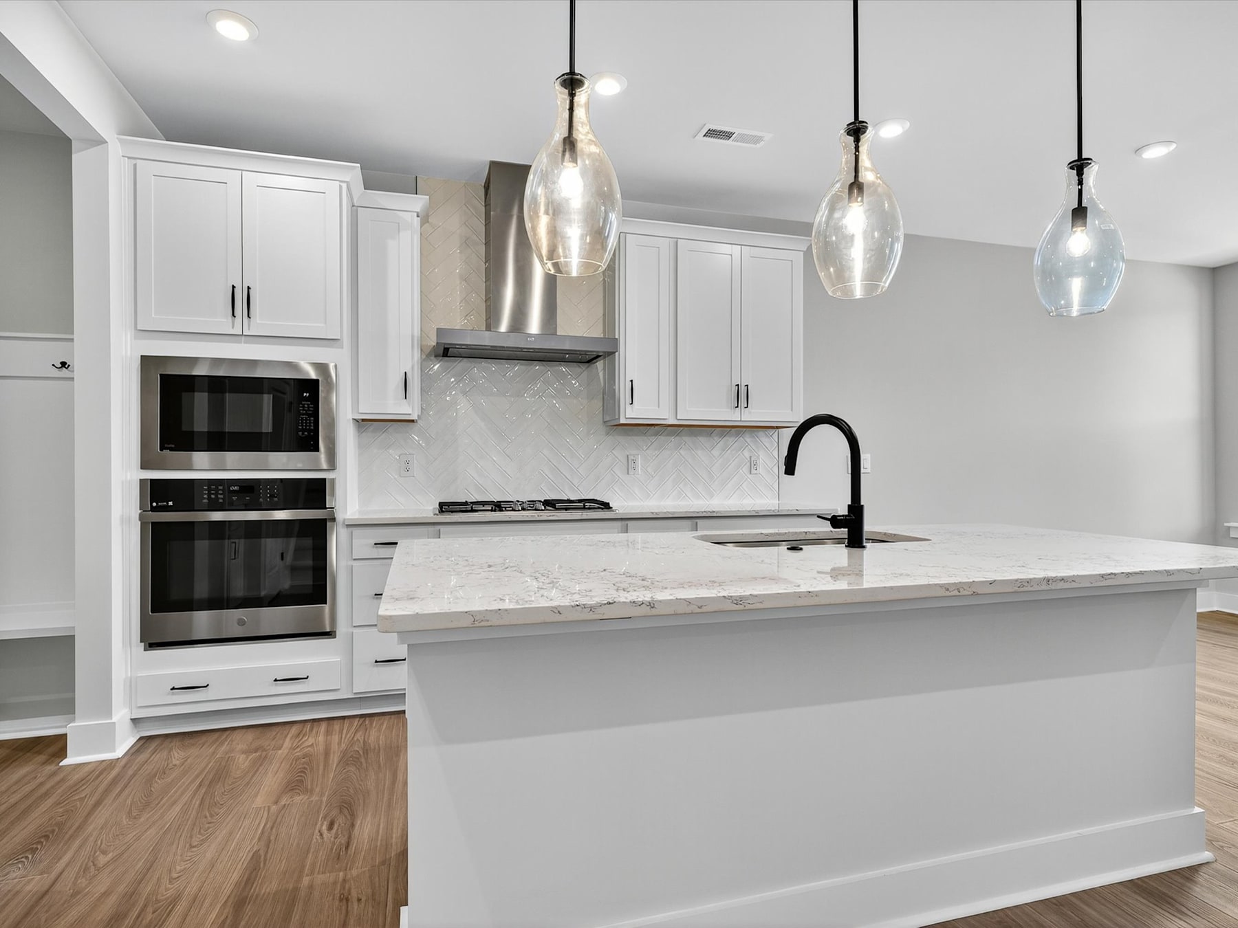 A modern, bright kitchen with white cabinets, a marble countertop, and pendant lights hanging above the island.