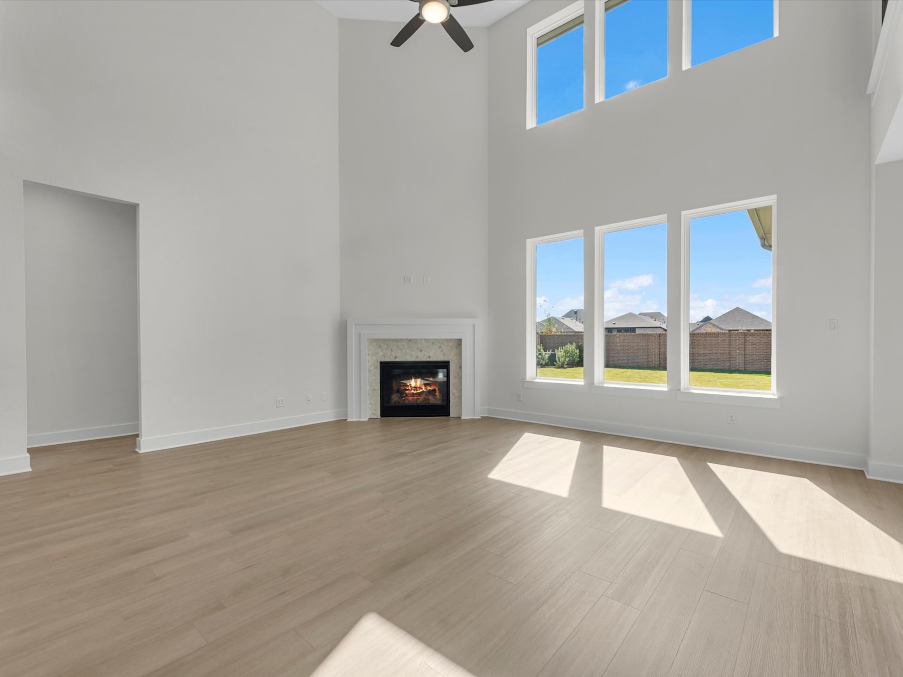 A spacious and bright living room with a fireplace, hardwood floors, and large windows overlooking a scenic outdoor landscape.