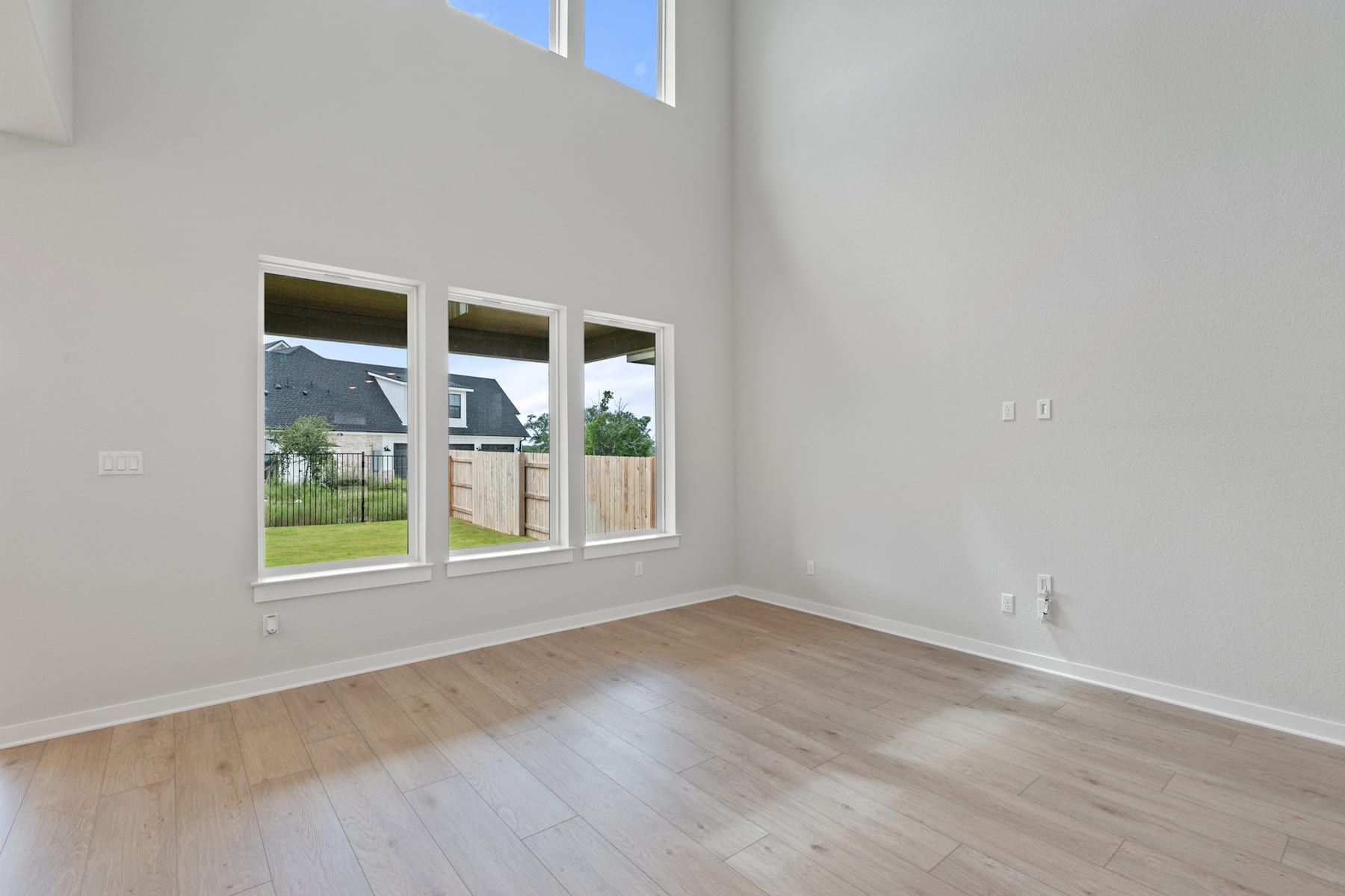A spacious, bright room with large windows overlooking a residential area, featuring hardwood floors and a minimalist, neutral-toned interior design.