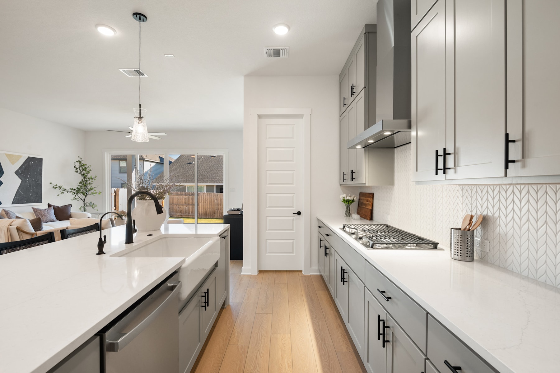 A modern, minimalist kitchen with white countertops, gray cabinets, and a sleek, open layout that extends into a living area with a couch and artwork on the walls.