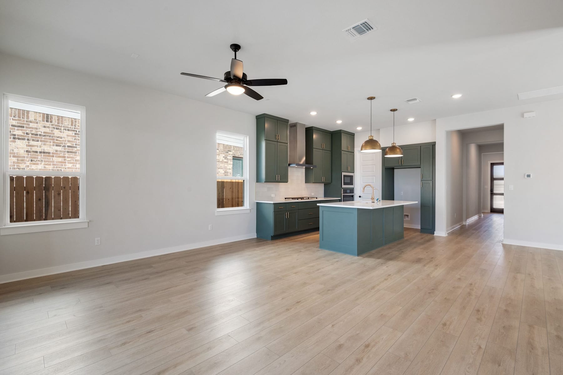 A modern, open-concept kitchen and living room with hardwood floors, a ceiling fan, and a mix of light and dark cabinetry.