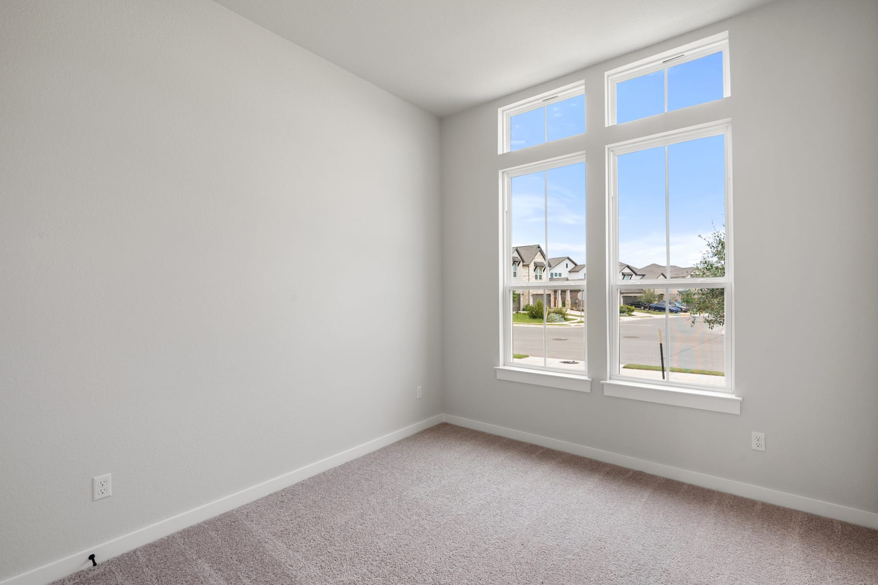 A bright and spacious room with large windows overlooking a residential neighborhood in the background.