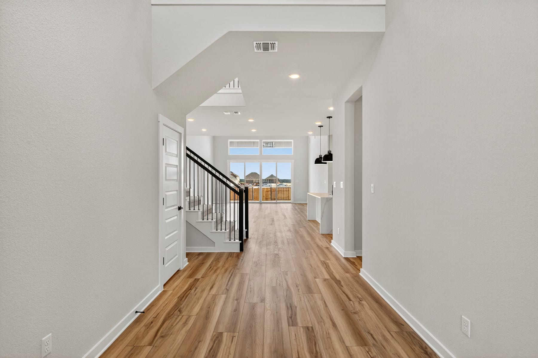 A bright and spacious hallway with a wooden floor, leading to a room with a window in the background.