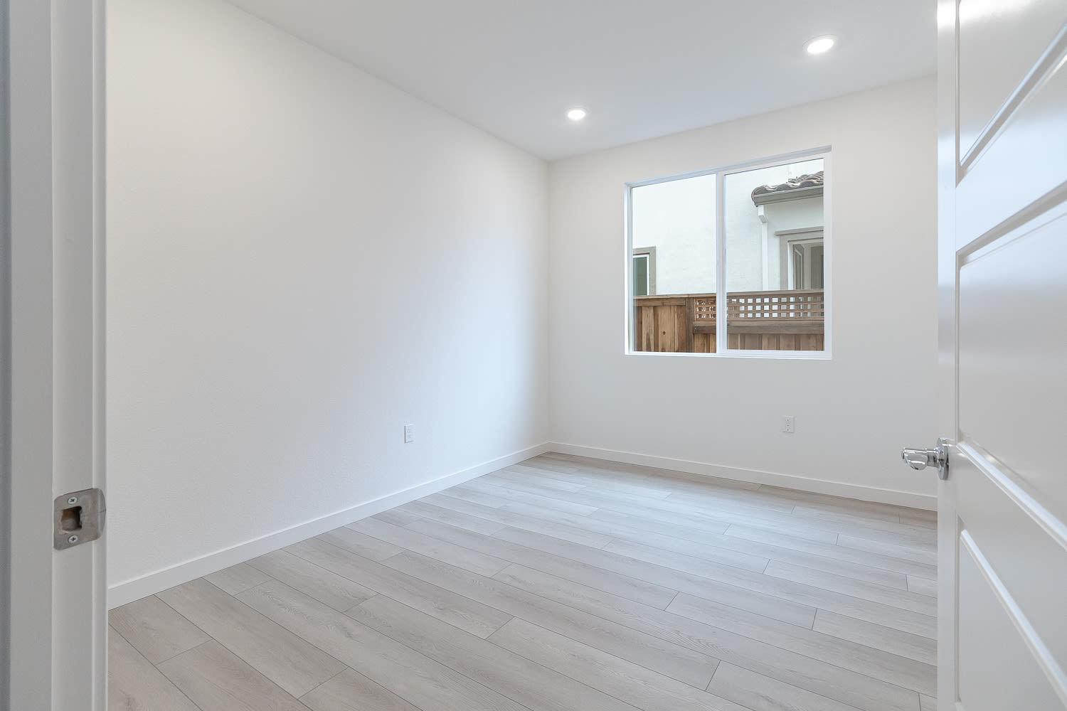 A bright, minimalist room with white walls and a wooden floor, featuring a window that provides natural light.