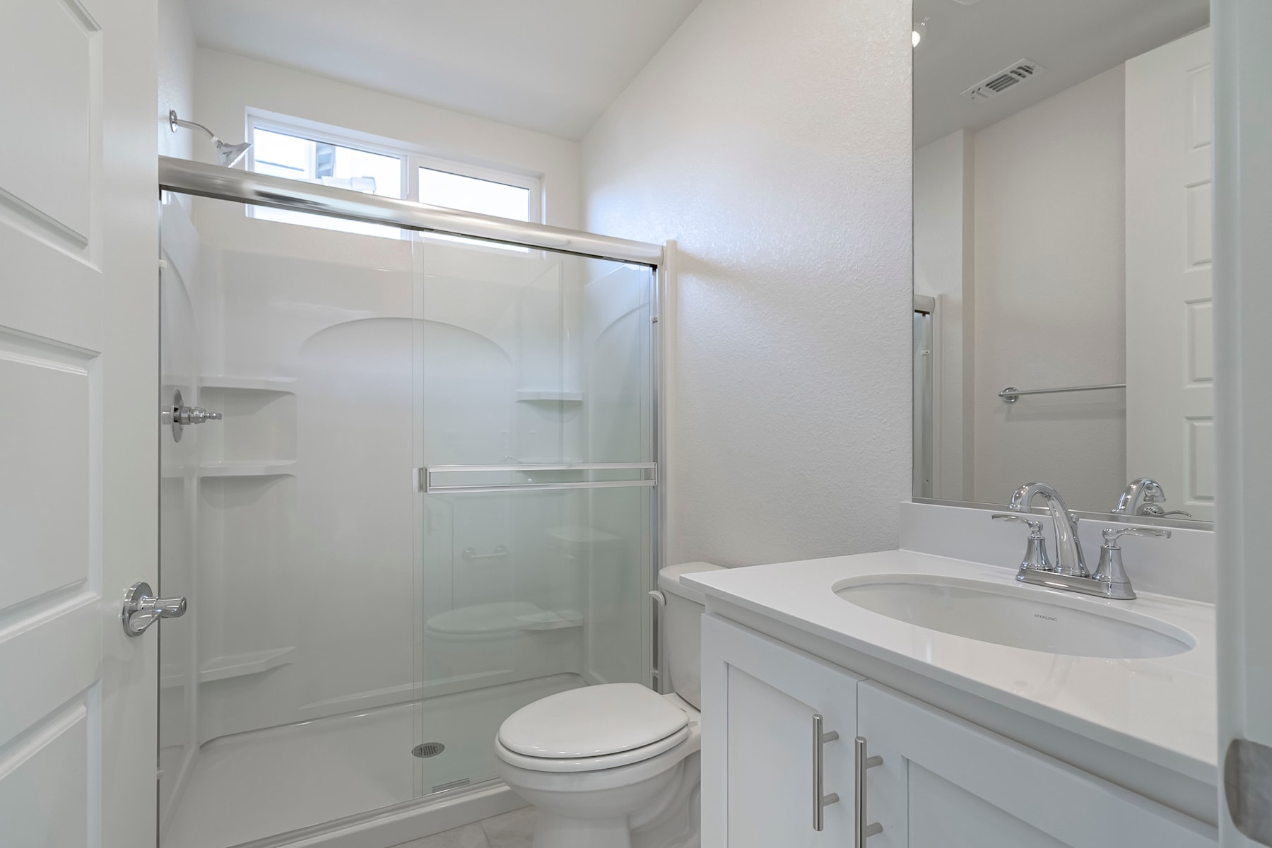 A modern, well-lit bathroom with a white vanity, a glass-enclosed shower, and a toilet. The room appears clean and minimalist in design.