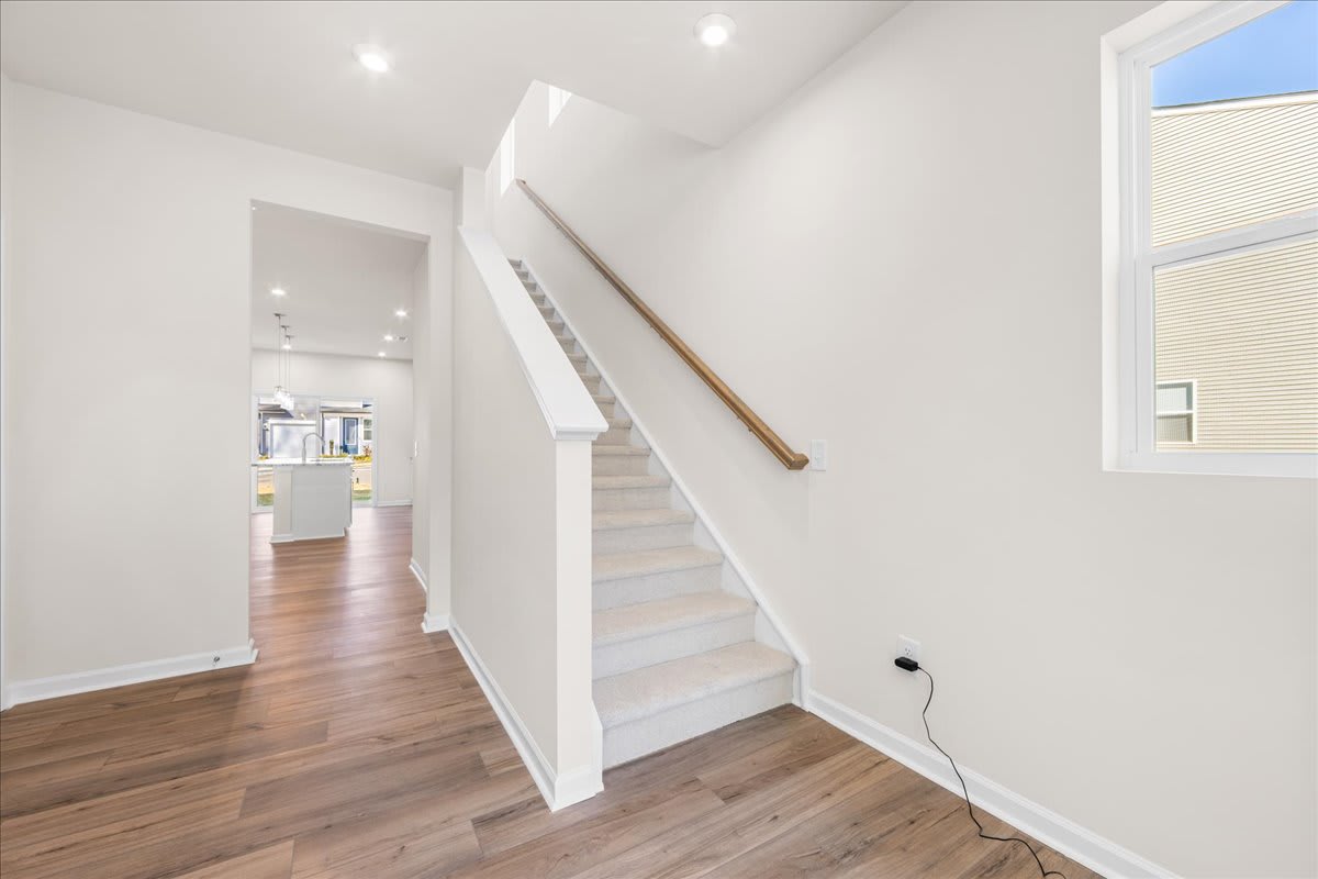 A bright and spacious interior with a wooden staircase leading up to the second floor, surrounded by white walls and a large window providing natural light.