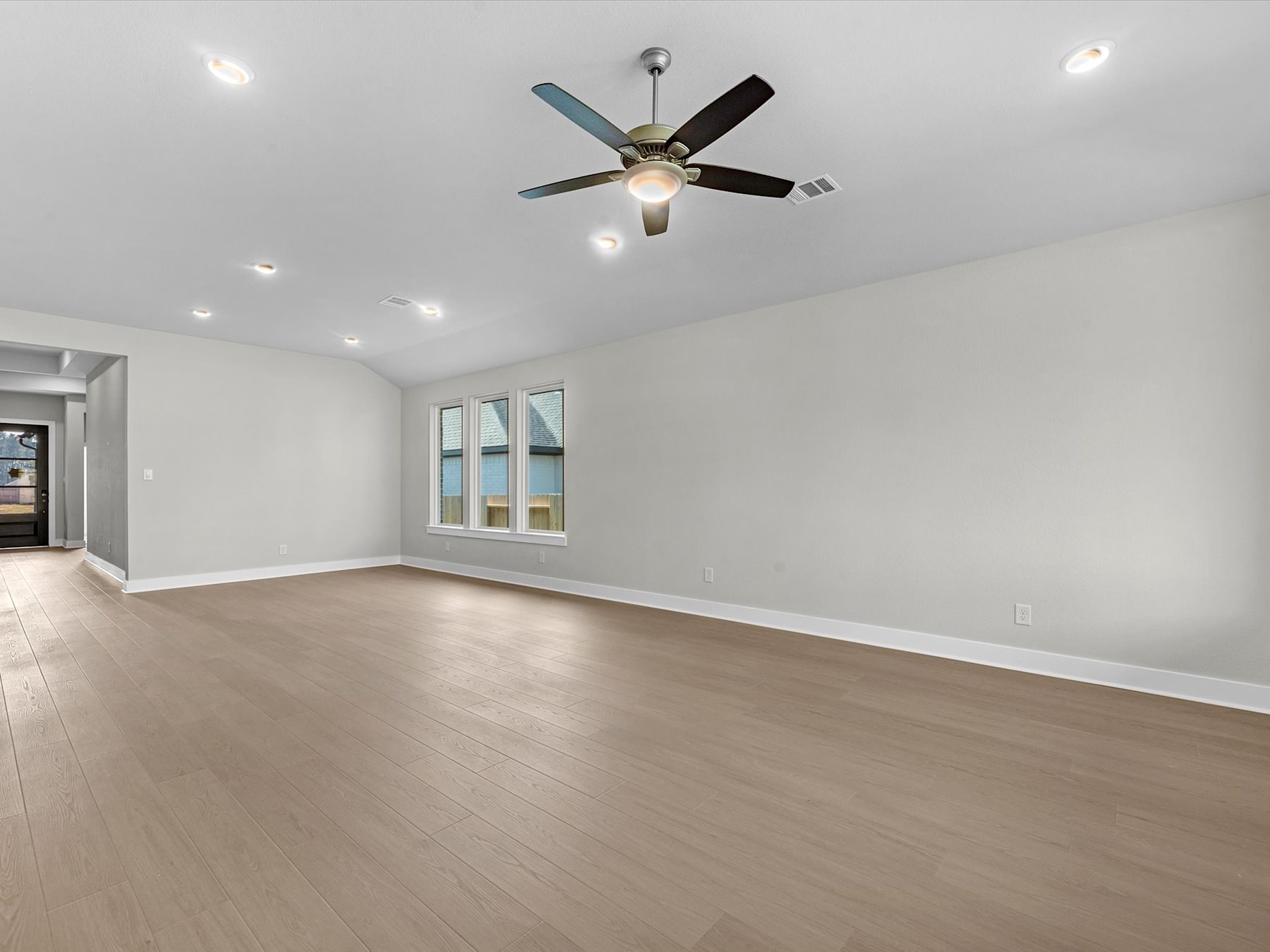 A spacious, well-lit room with a ceiling fan and hardwood flooring, providing a clean and modern atmosphere.