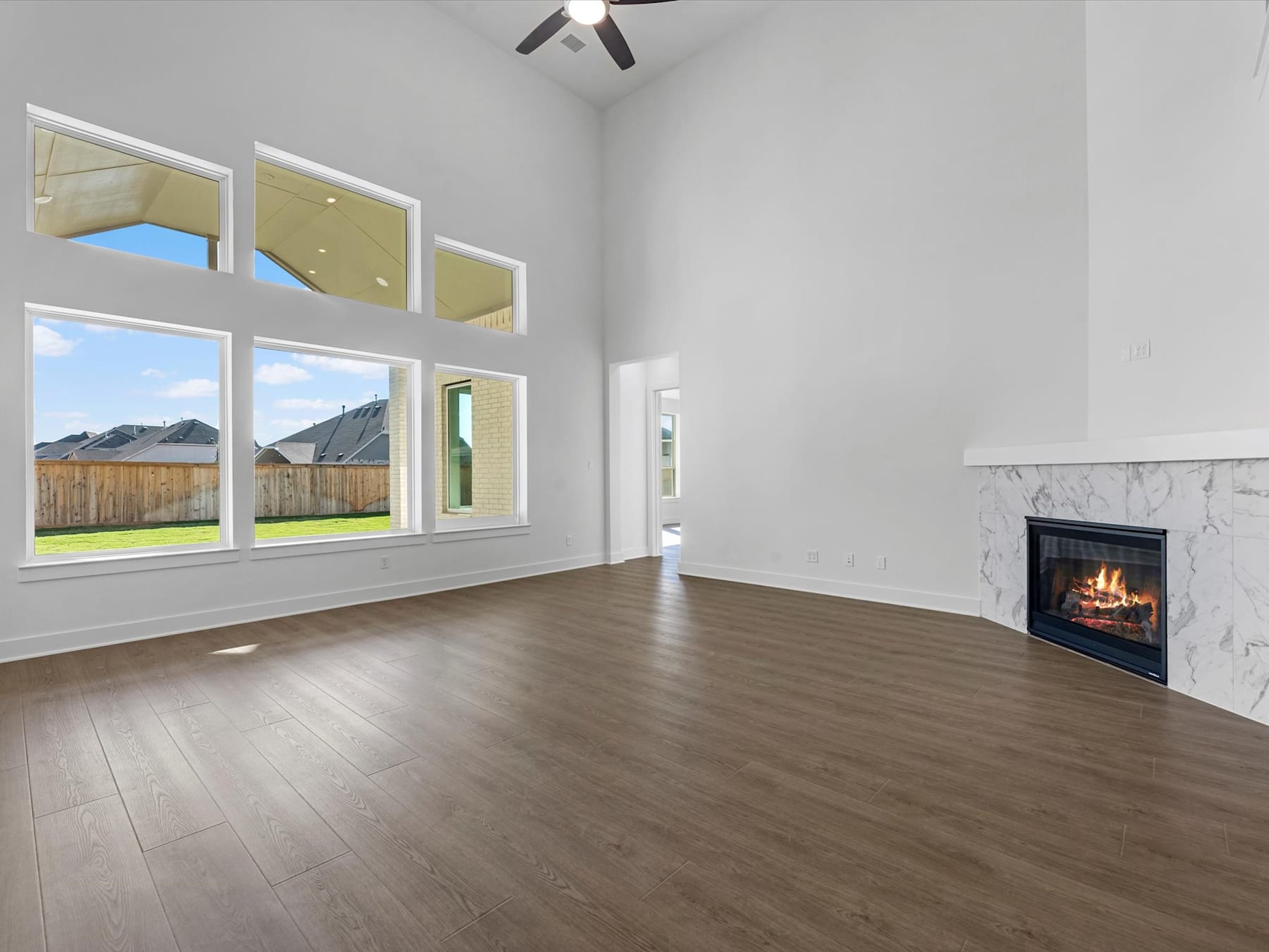 A spacious and modern living room with large windows overlooking a backyard, featuring a fireplace and hardwood flooring.