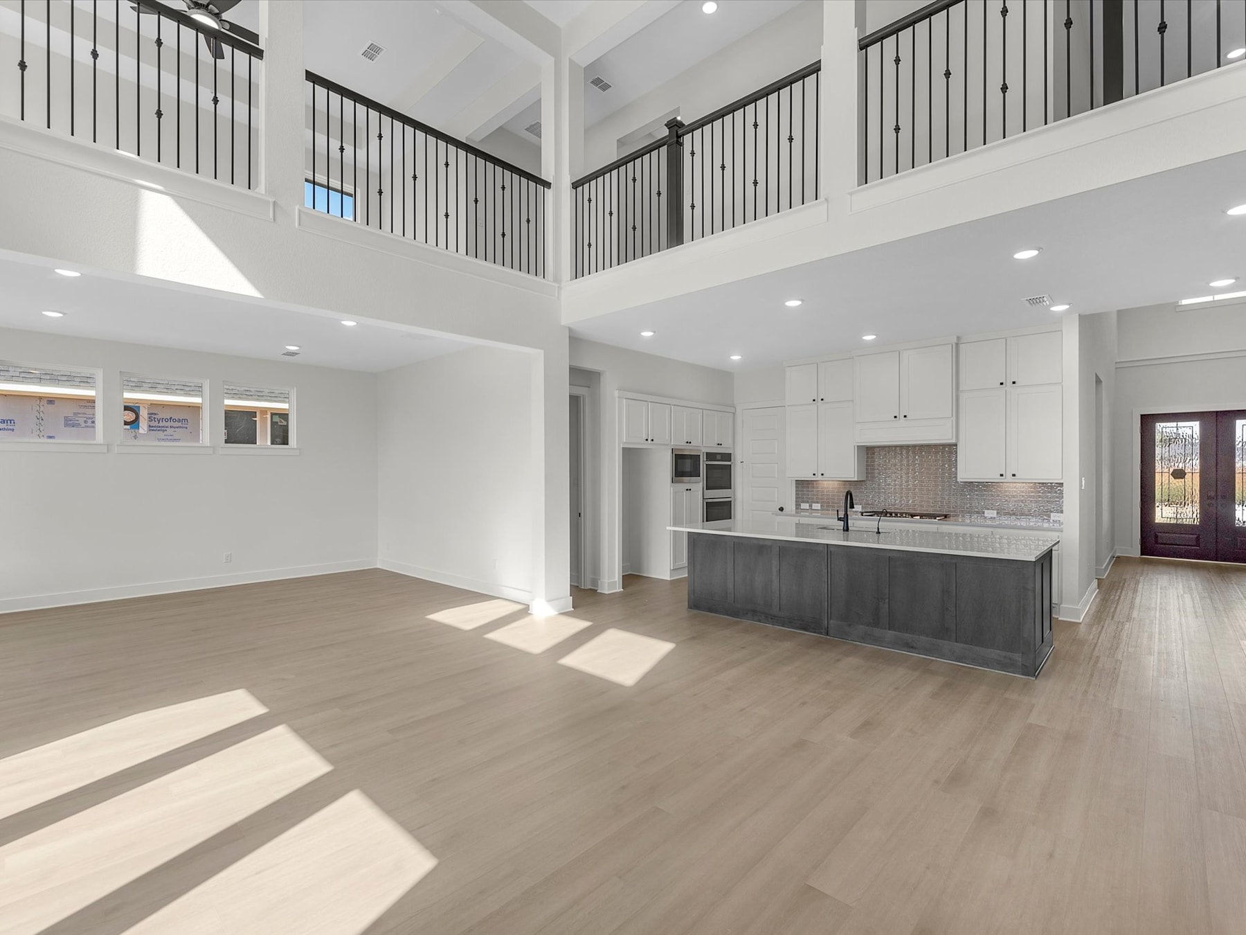 A spacious, open-concept living area with a high ceiling, hardwood floors, and a modern kitchen visible in the background.