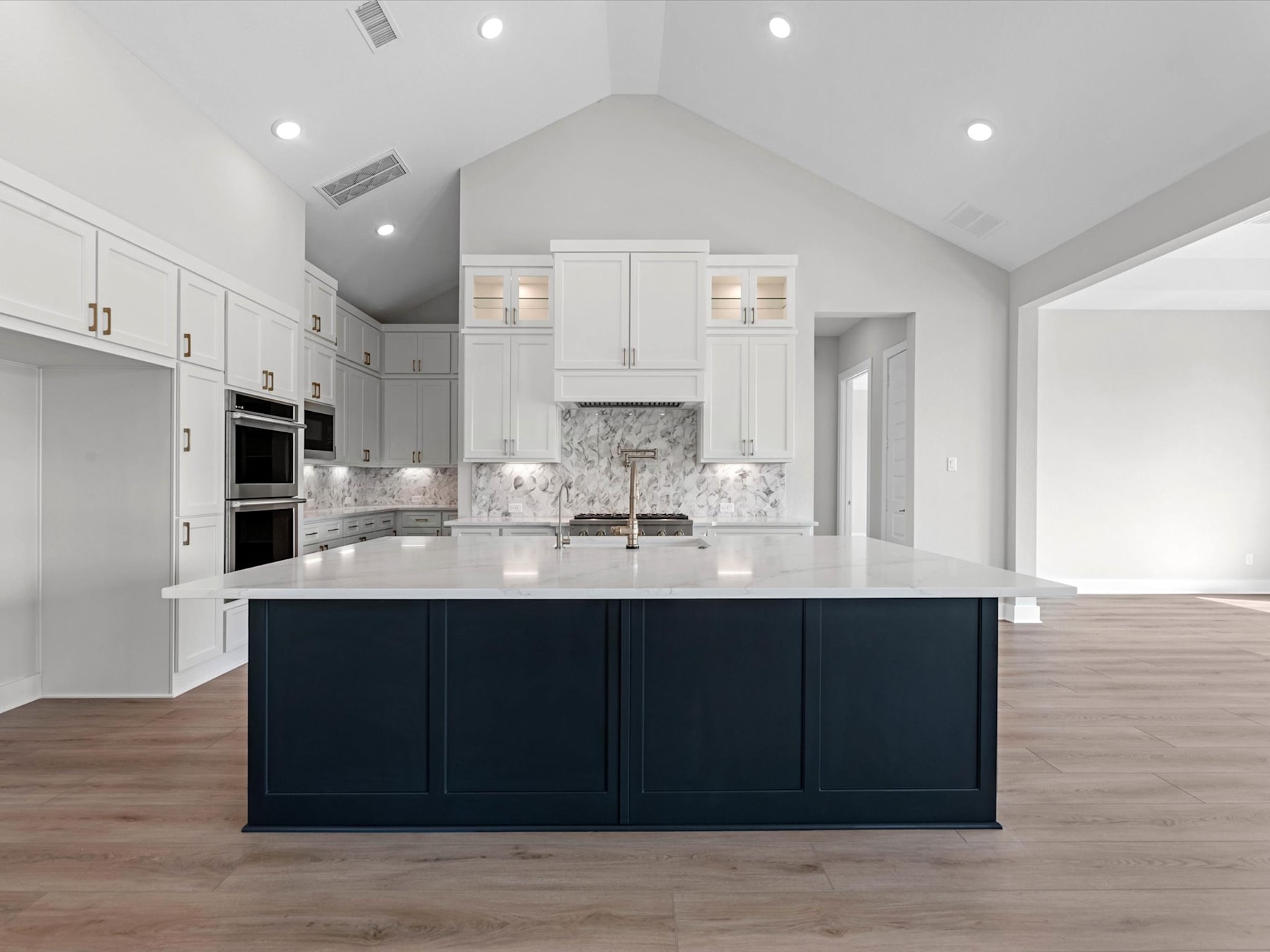 A modern, spacious kitchen with white cabinets, a large black island, and a marble backsplash, set against a bright and airy background.