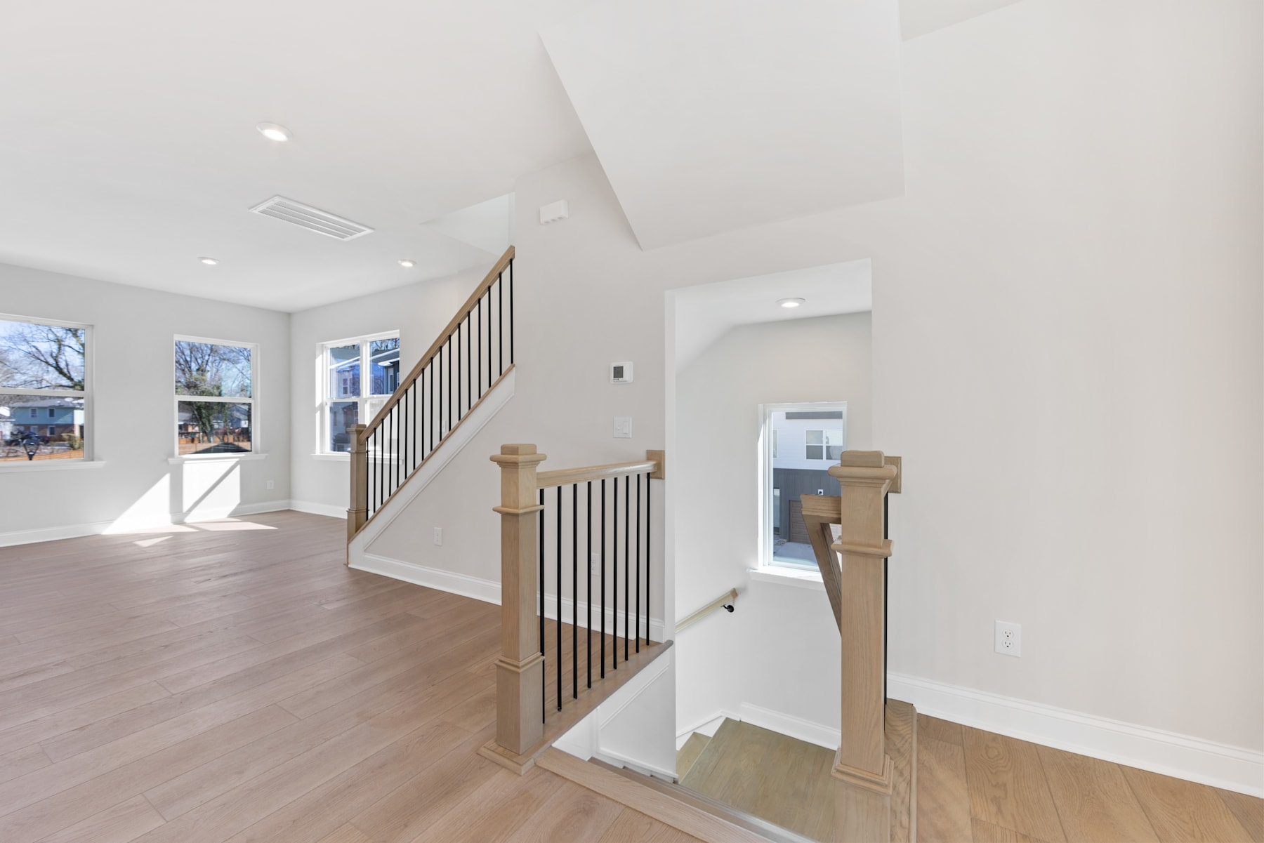 A bright and airy interior with a wooden staircase and railing leading to an upper level, surrounded by white walls and hardwood floors.