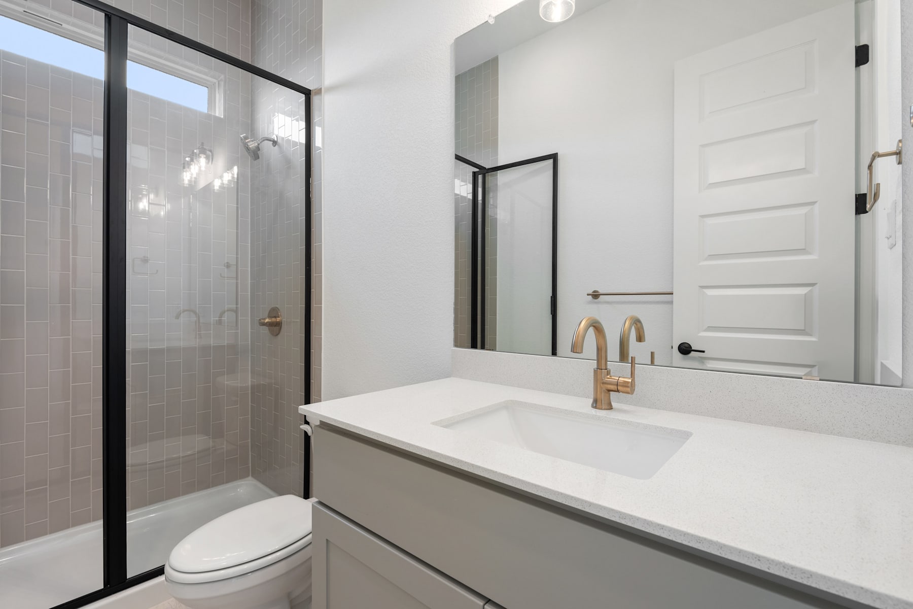 A modern, minimalist bathroom with a white vanity, black framed mirror, and a glass shower enclosure.