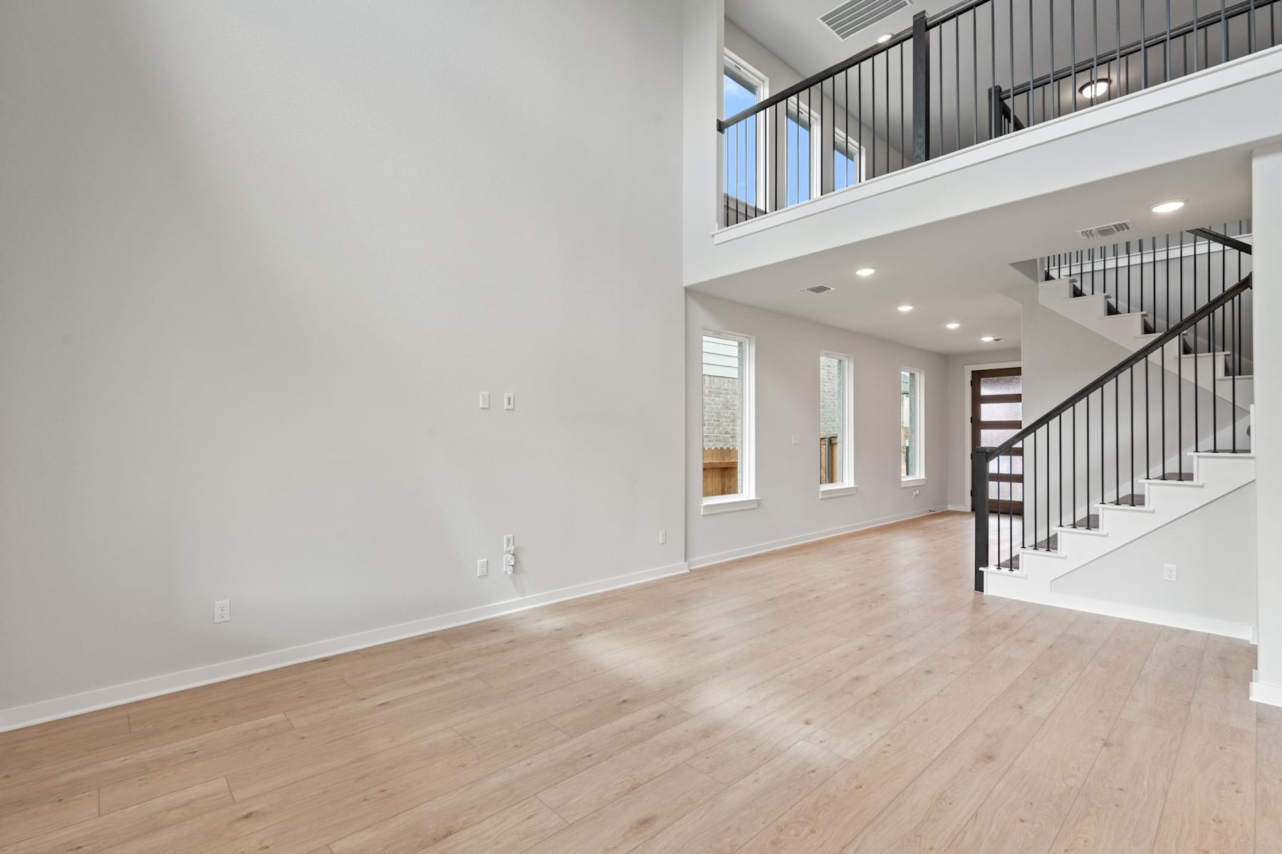 A spacious and bright interior with hardwood floors, a staircase, and large windows providing natural light.