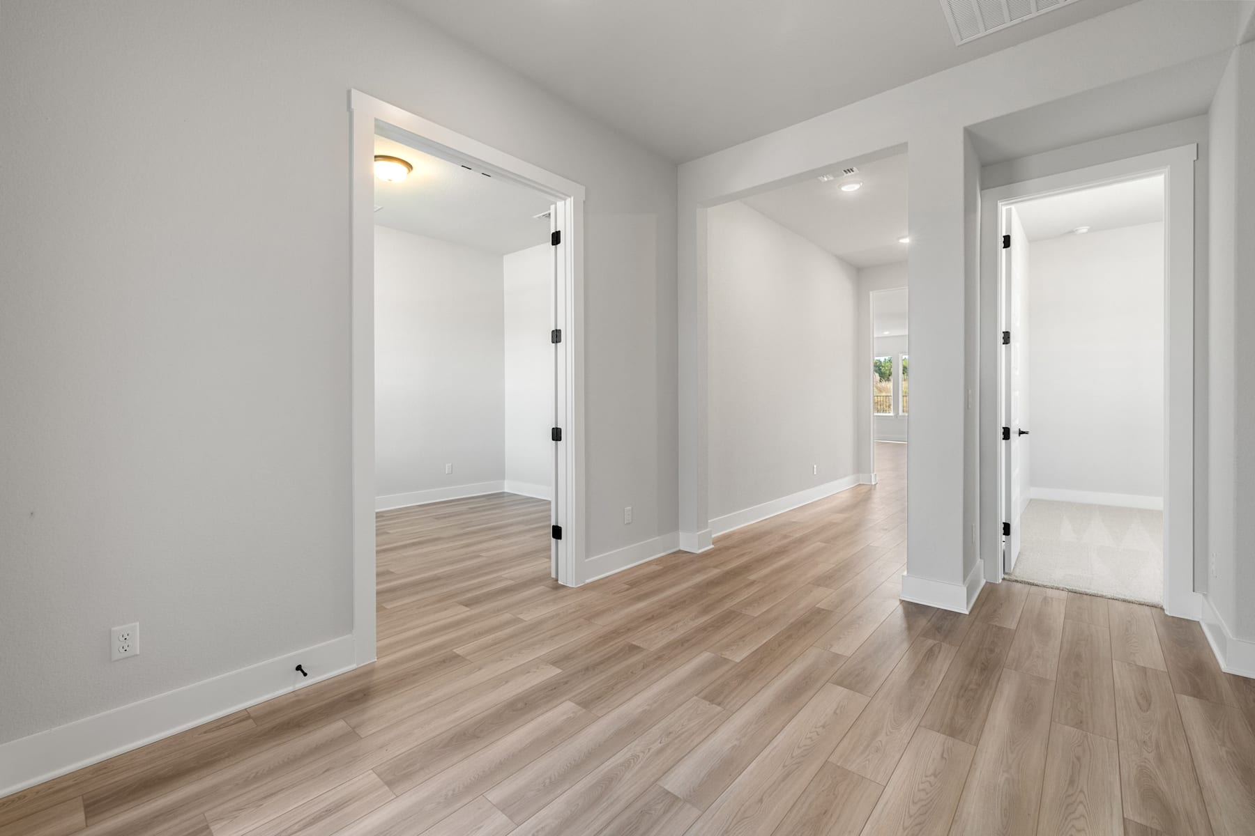 A bright, spacious hallway with white walls and light-colored hardwood floors, leading to several open doorways.