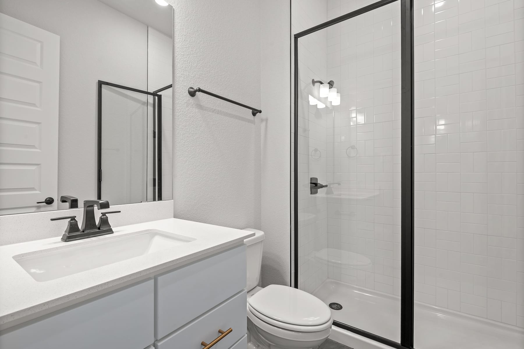 A modern, minimalist bathroom with a white vanity, a frameless glass shower enclosure, and a toilet in the background.