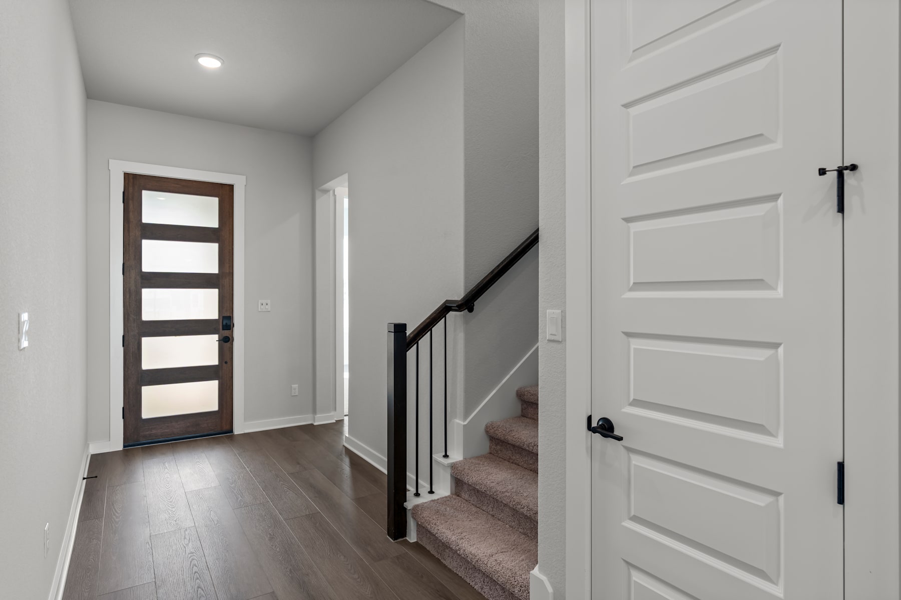 A modern, minimalist entryway with a wooden door, white walls, and a staircase leading upstairs.
