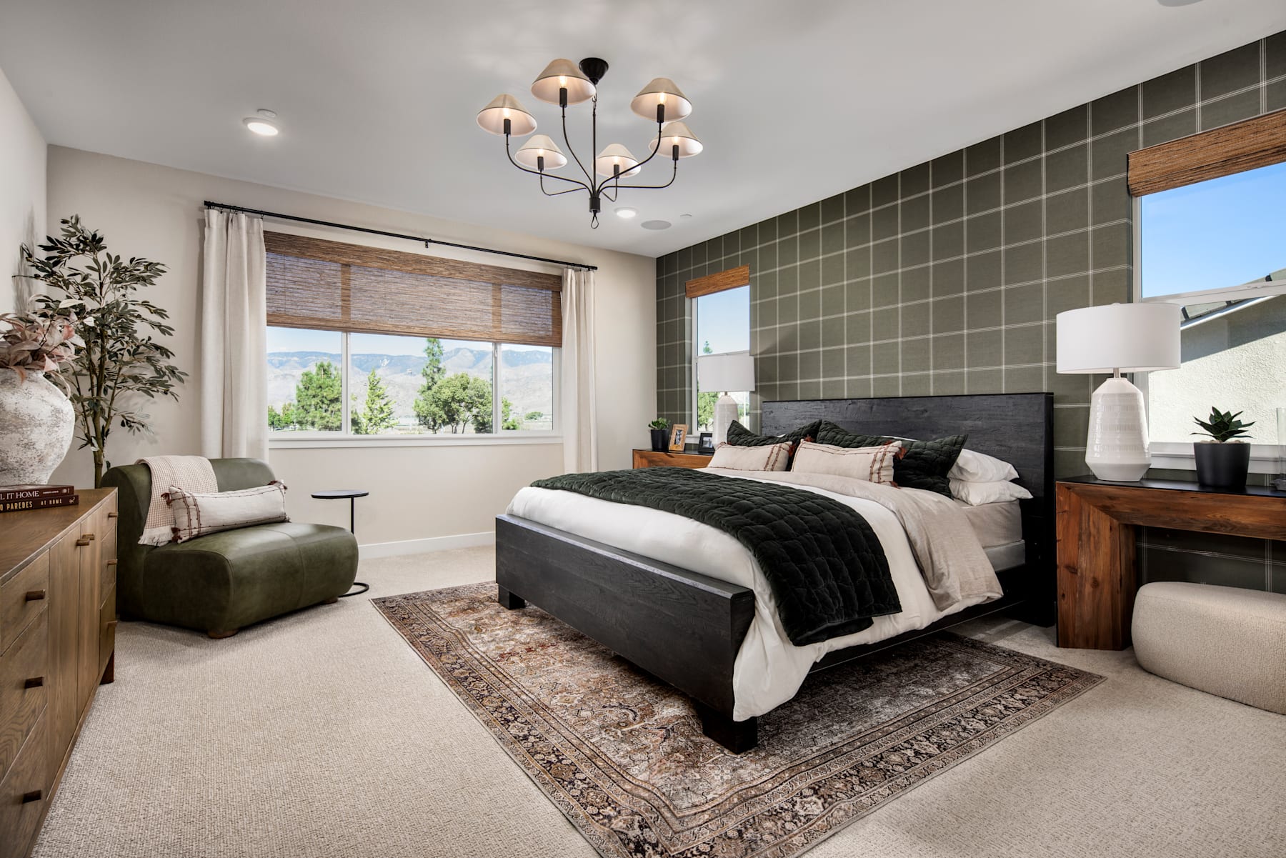 A cozy and well-designed bedroom with a large bed, wooden furniture, and a chandelier, set against a backdrop of patterned walls and a window overlooking a scenic outdoor view.