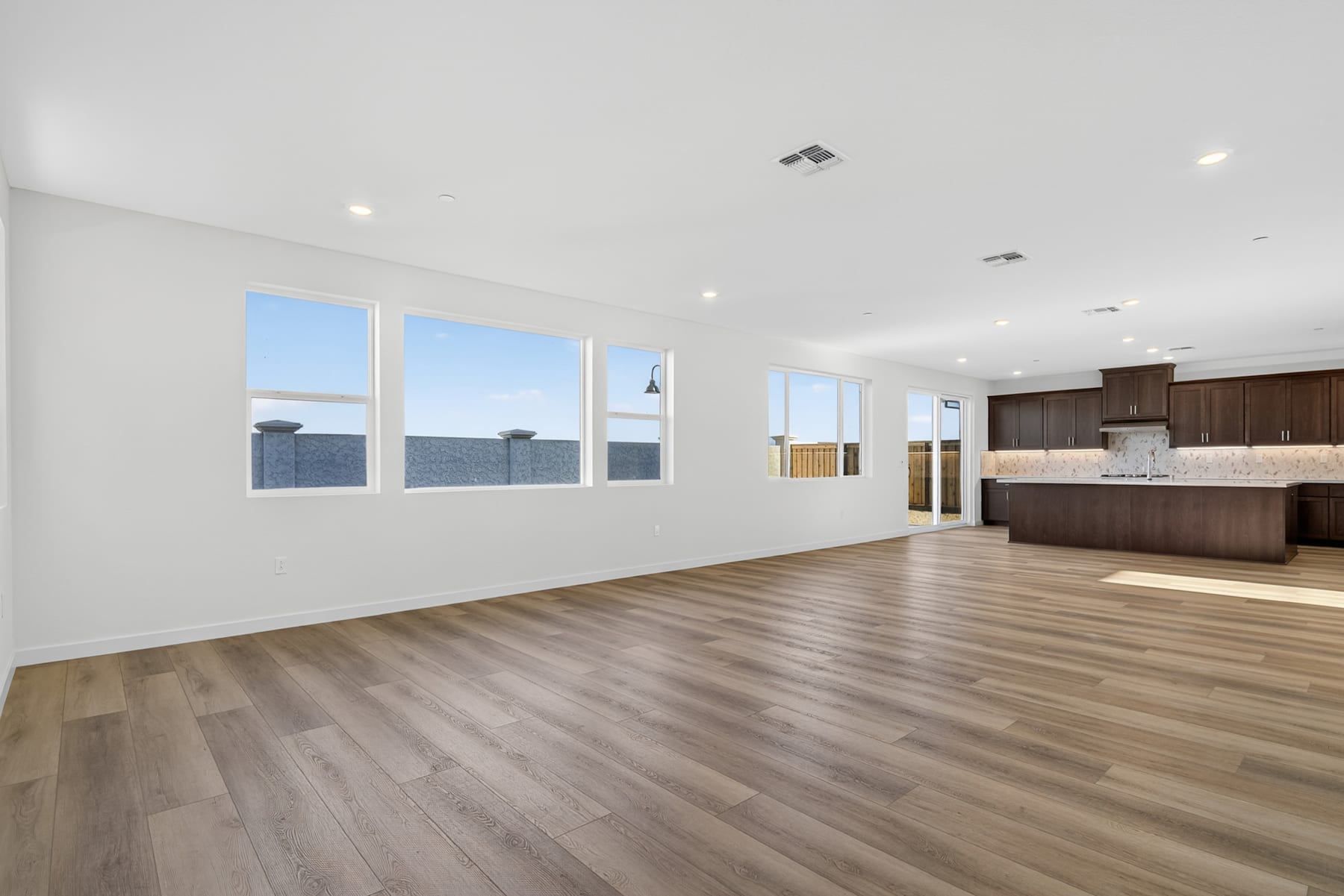 A spacious, open-concept living area with large windows, hardwood floors, and a modern kitchen visible in the background.