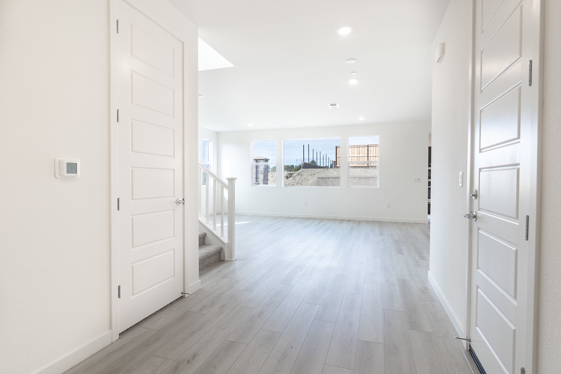 A bright, spacious hallway with white walls and wooden floors, leading to a room in the background.